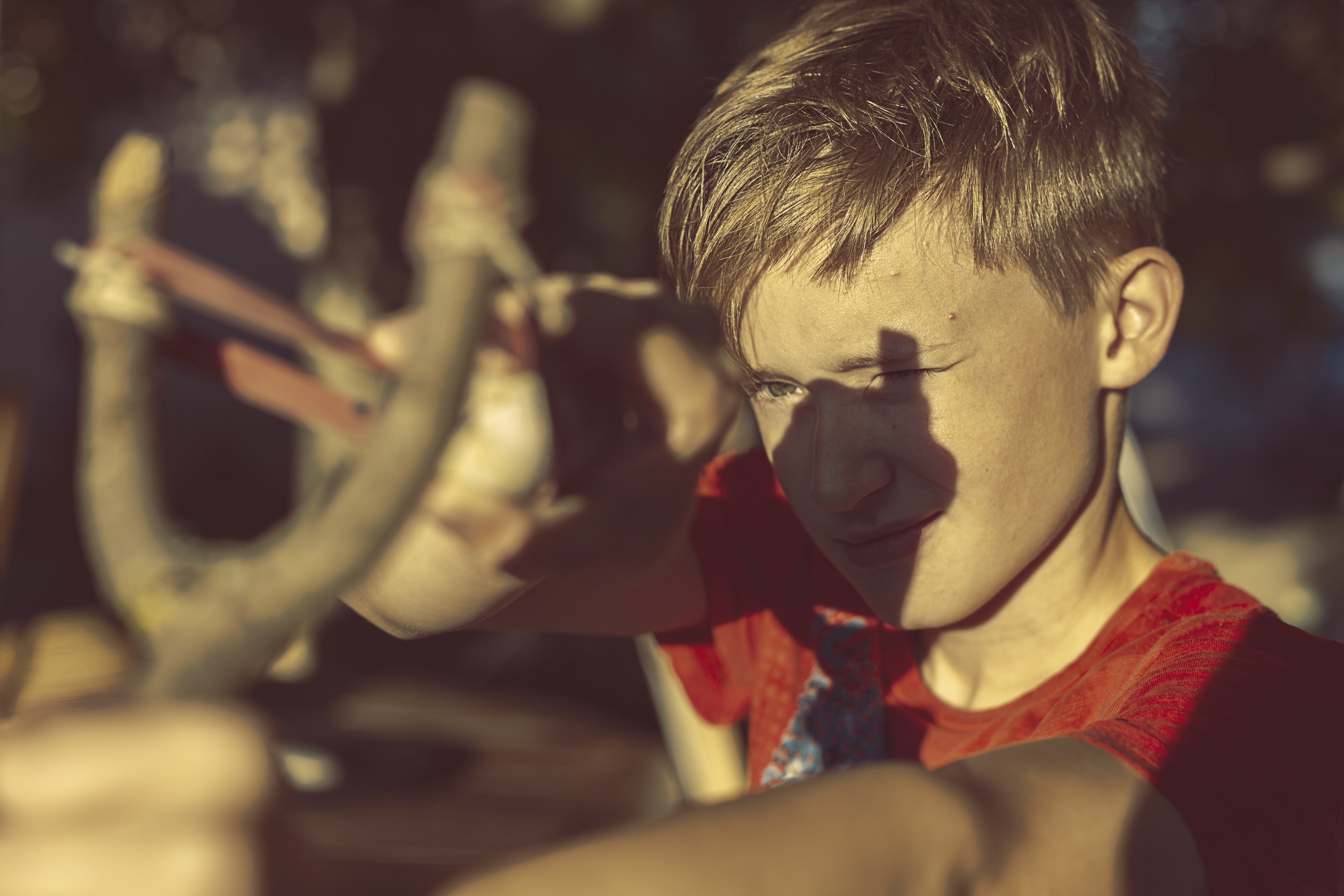 Boy using slingshot against sunbeam.