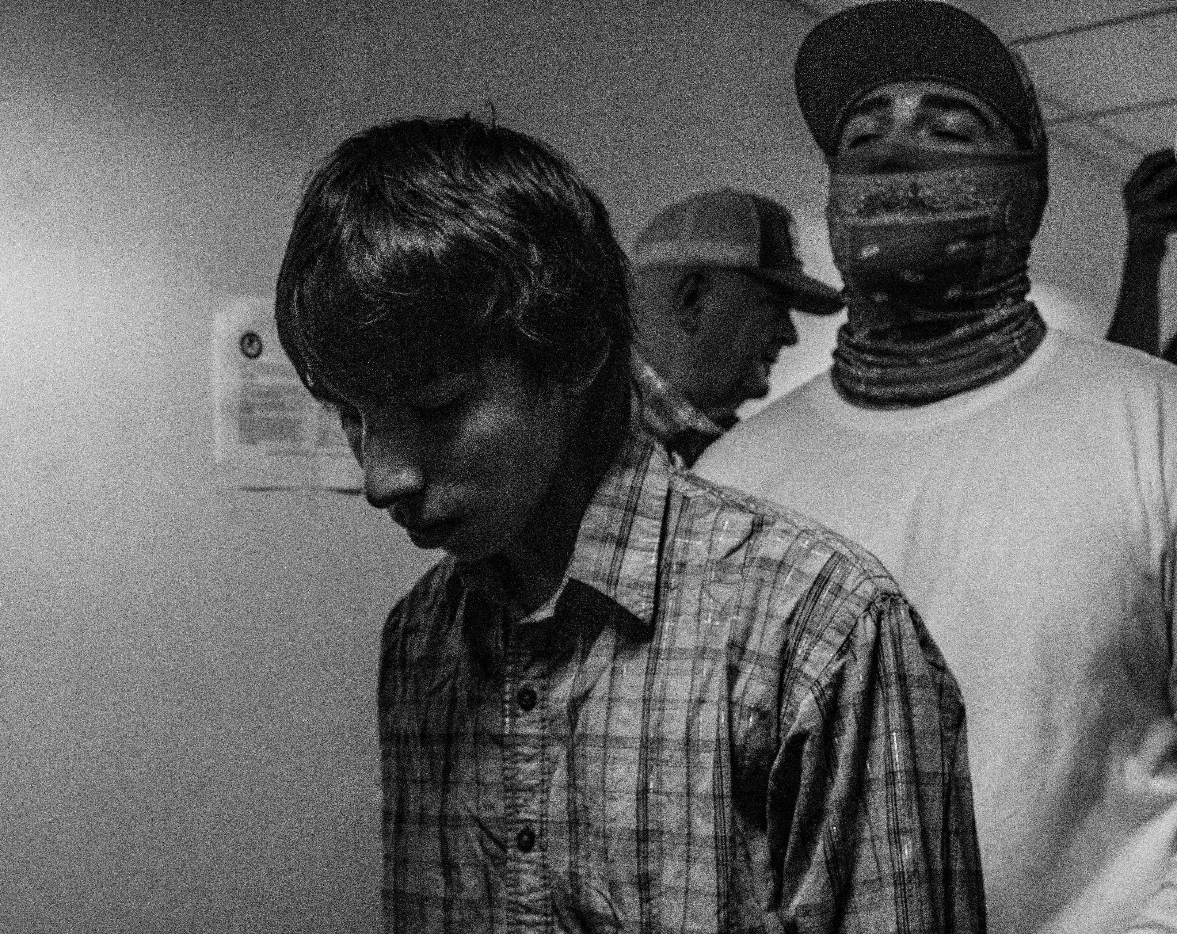 A young man is detained in the hallways of 26 Federal plaza with a federal agent following close behind him.