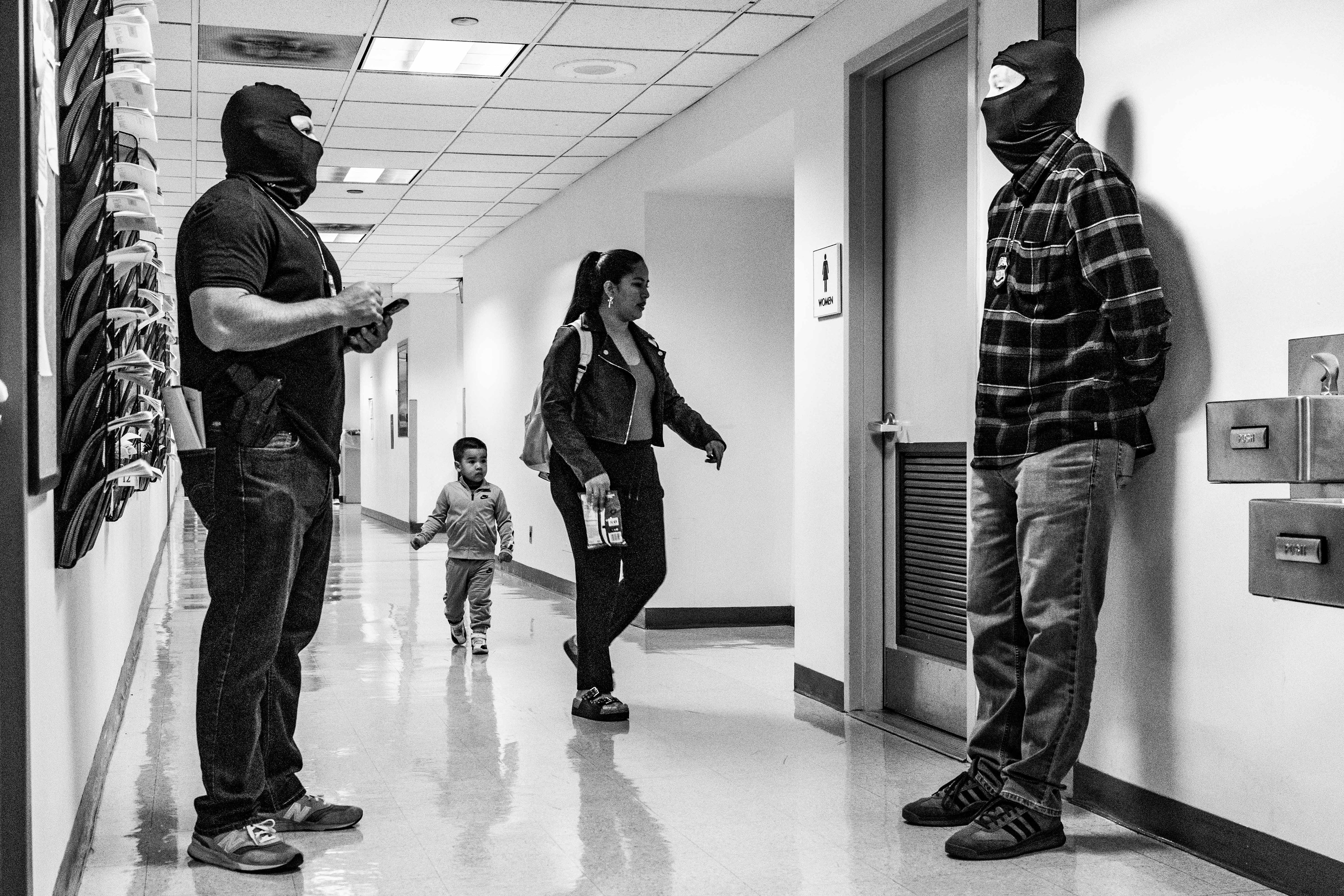 Agents stand idly in the hall as a mother and son walk towards the bathroom. 26 Federal Plaza is often times calm between detainments with many agents just standing around.