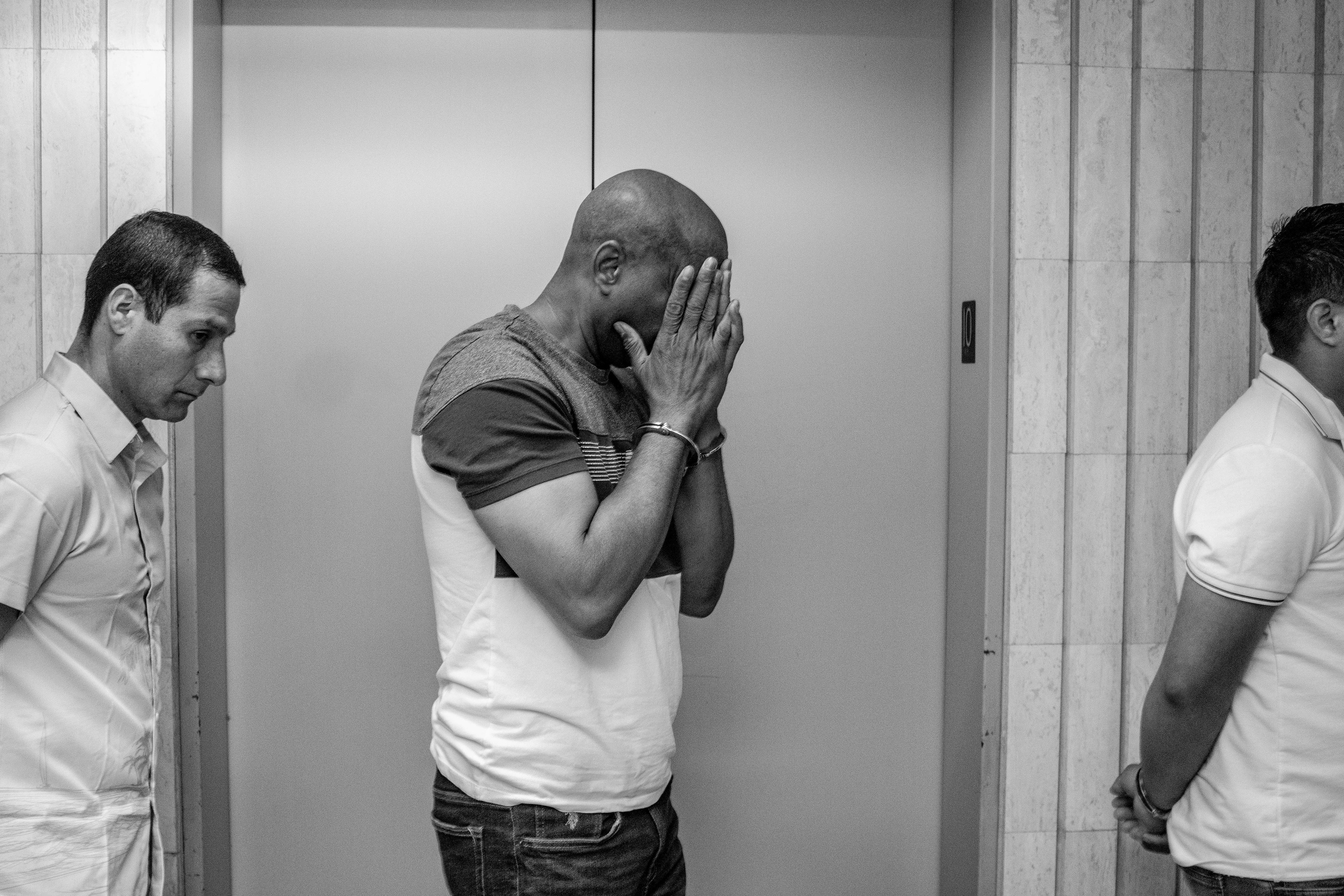 A group of detained immigrants are escorted in cuffs through the elevator bank into detention.
