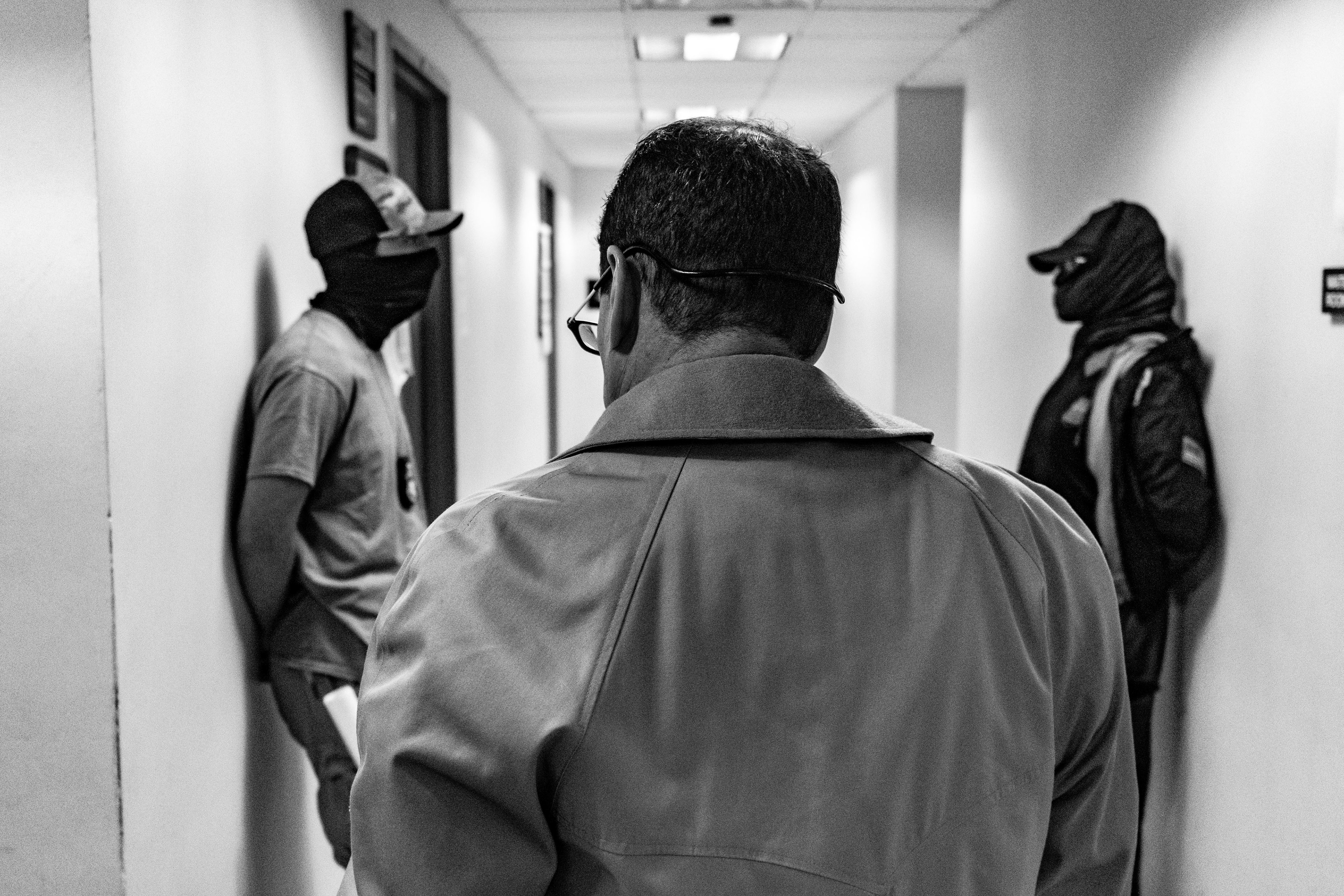 A lawyer exits a waiting room and encounters two masked federal agents waiting outside.