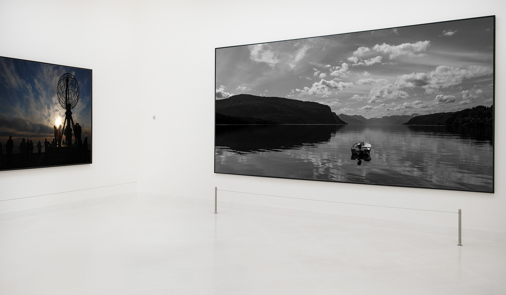 Wall image into a gallery, there are two images. One in Norway with clear mirror water reflecting the sky and the mountains into the horizon. A little boat is in the middle of the picture.