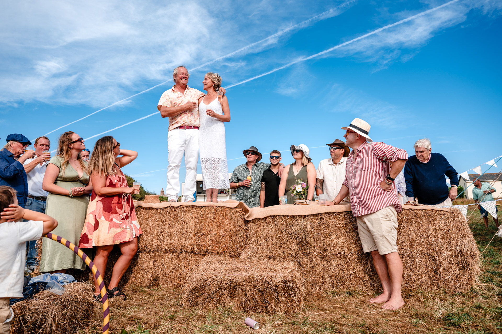 A bride and groom give a speech atop a hay bale during their Devon countryside wedding.