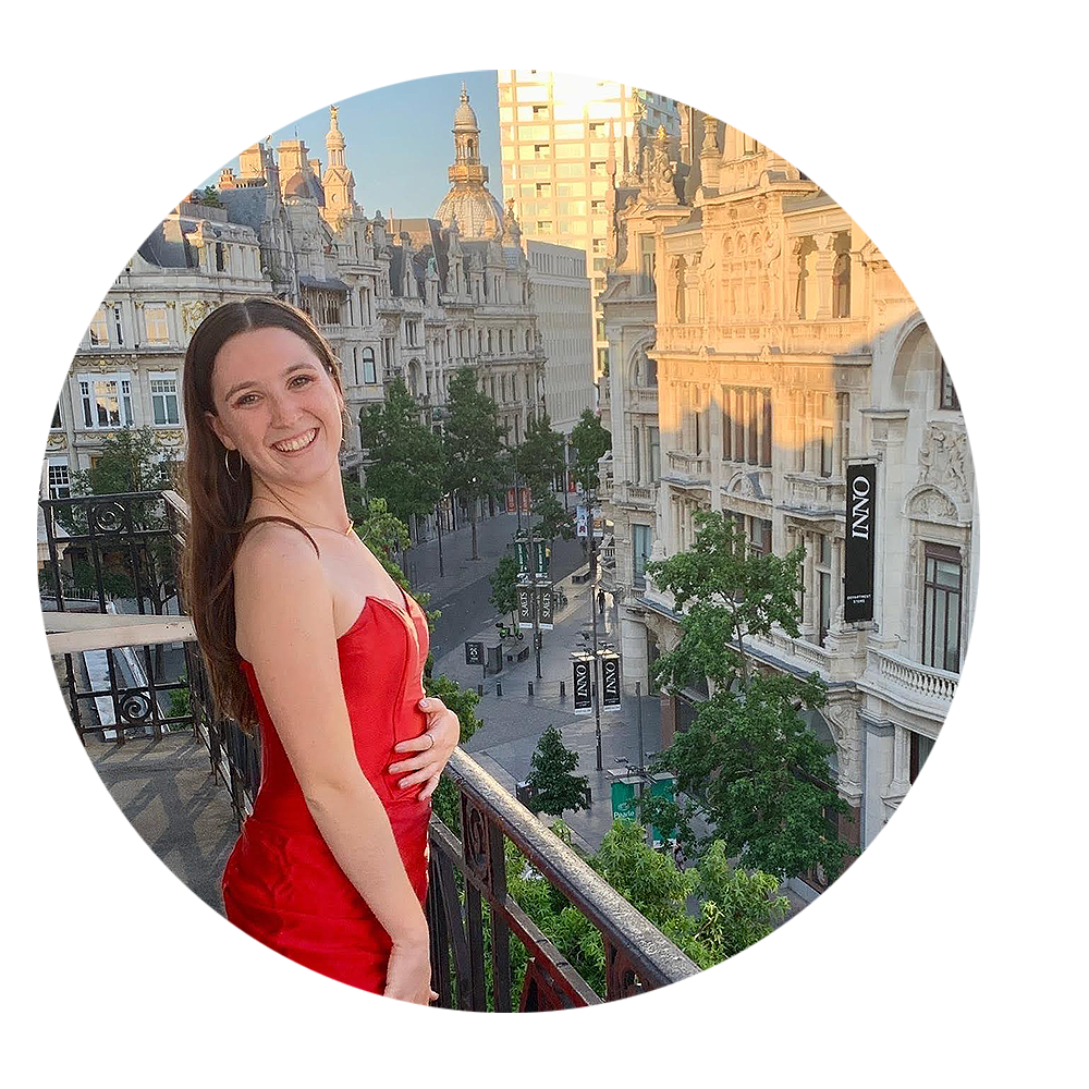Woman in Red dress standing on a balcony overlooking a shopping strip in Antwerp.