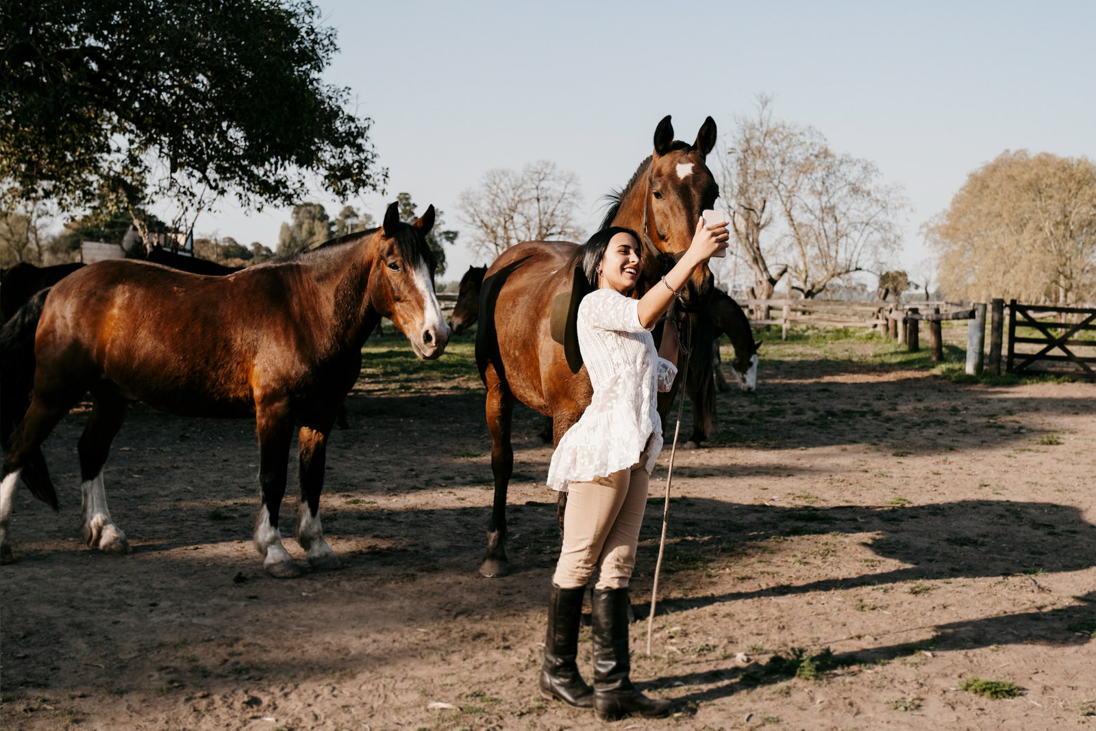 Woman taking a selfie with horses at a ranch, outdoor rural lifestyle