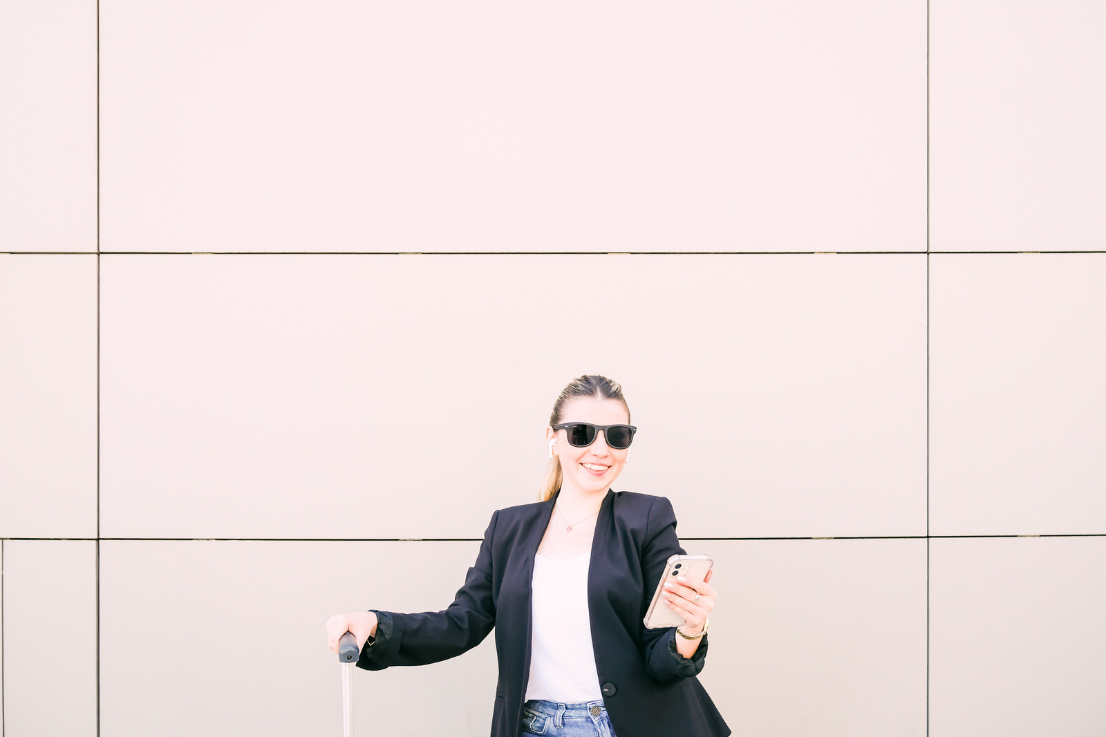 Young professional woman smiling while checking her phone and holding luggage, travel lifestyle