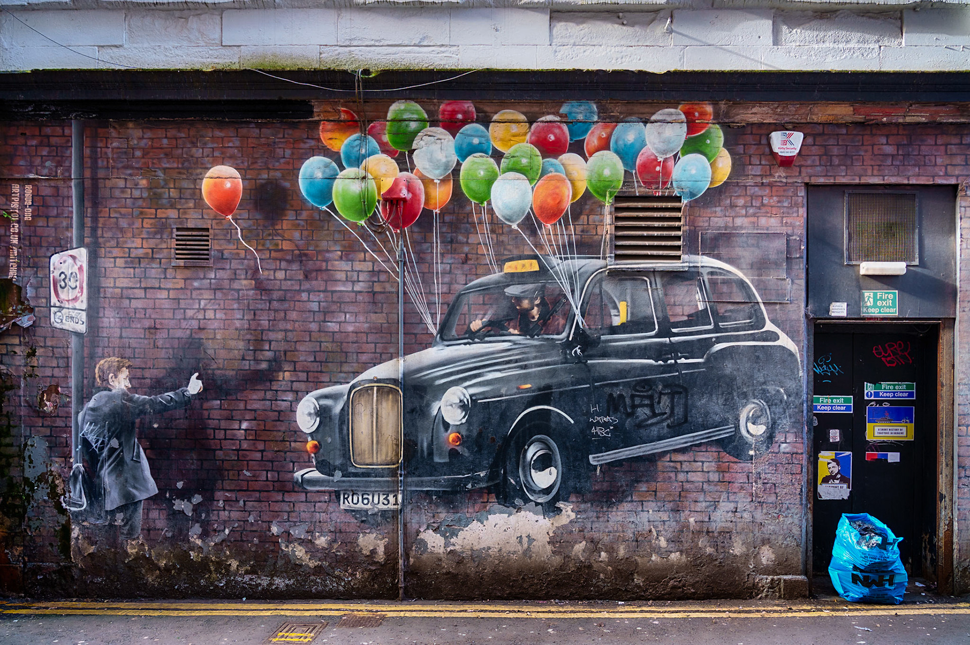 No. 12 in the Glasgow Mural Trail, The World's Most Economical Taxi by Rogue-One is painted in one of the city's alleys. The artist even painted a brick wall on the brisk wall for this one. The rubbish and the clutter has intentionally been included to reinforce the location.