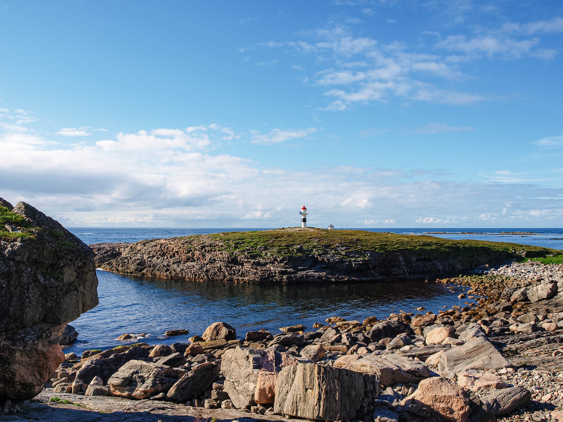 A lighthouse is visible from the winding Lofoten road