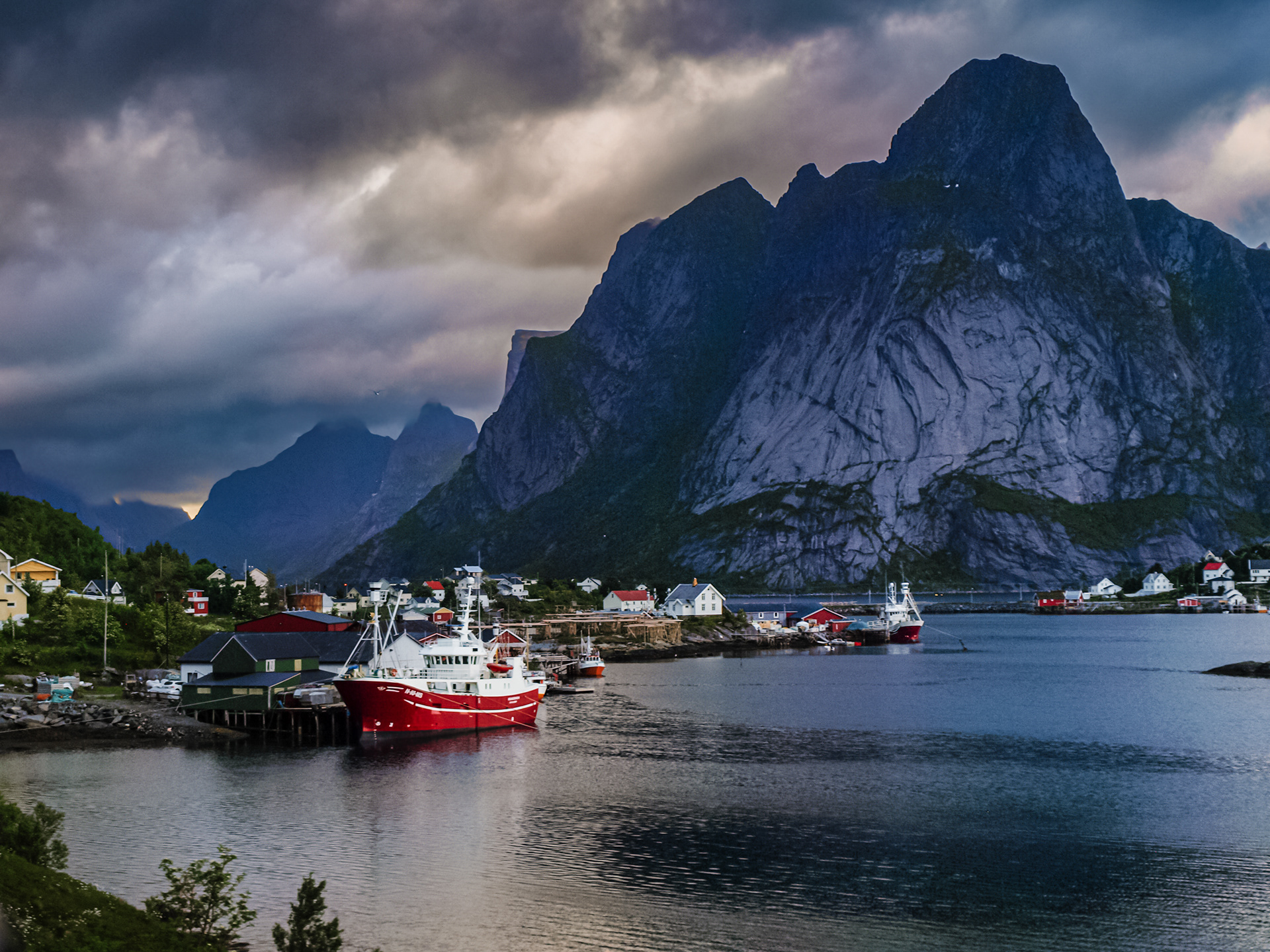 A massive peak looms over bright red boats docked in the town of Reine, Lofoten