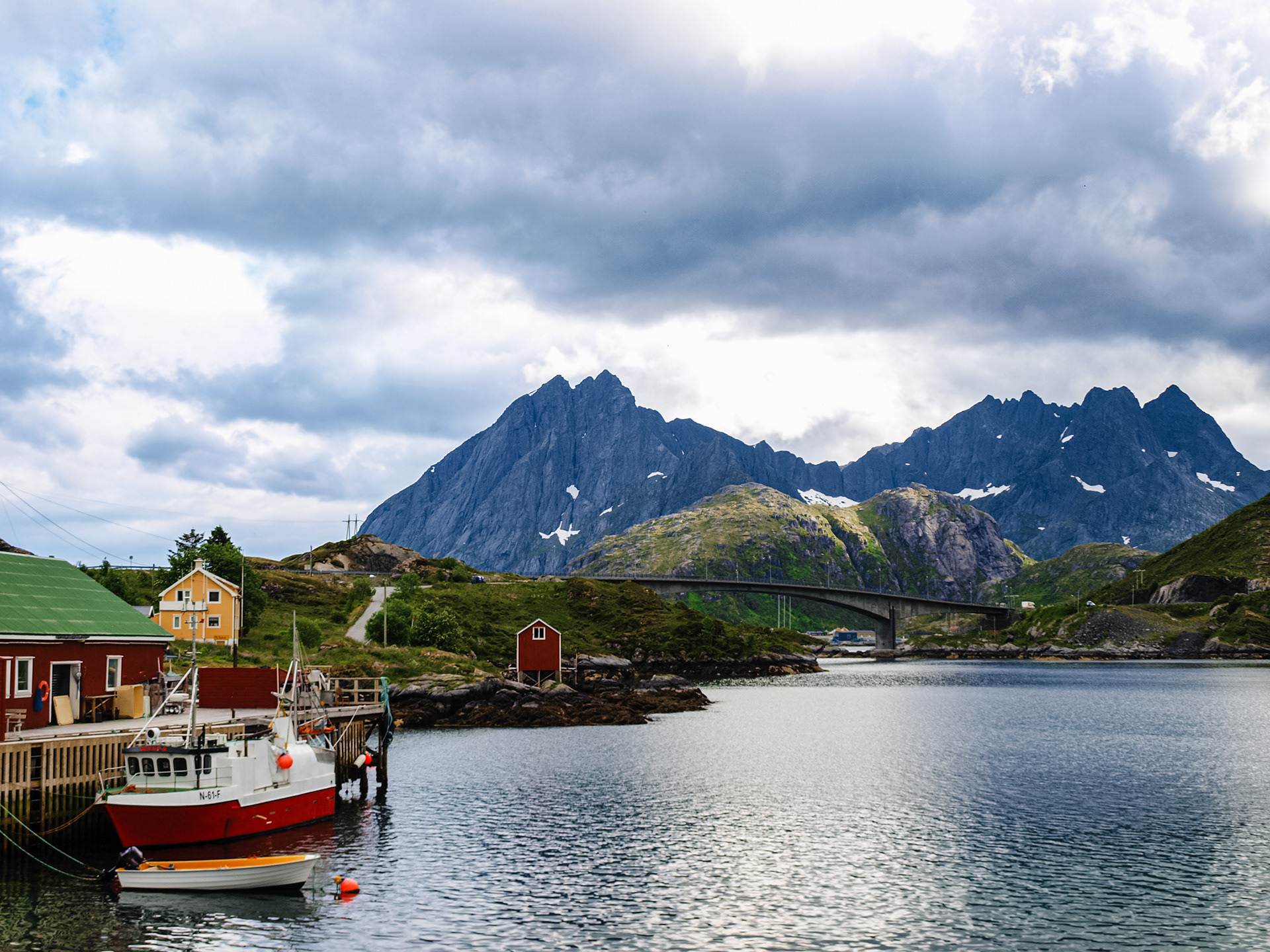A fishing boat is docked near a raised bridge with jagged peaks visible behind