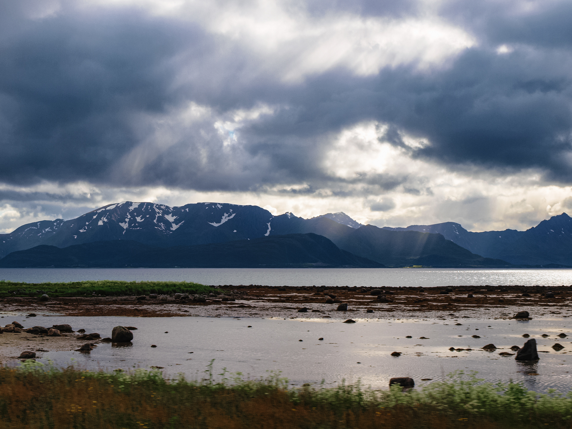Sun rays break through the cloud cover along the winding Lofoten road