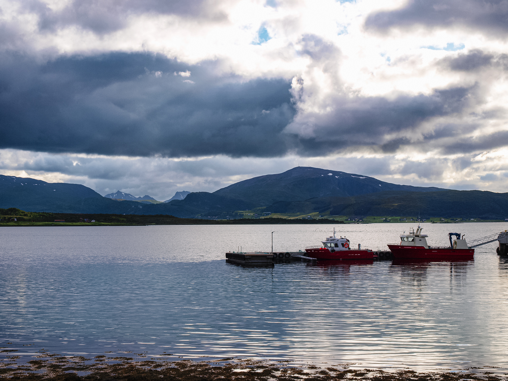 Fishing boats are docked near the road with sun rays visible in the background