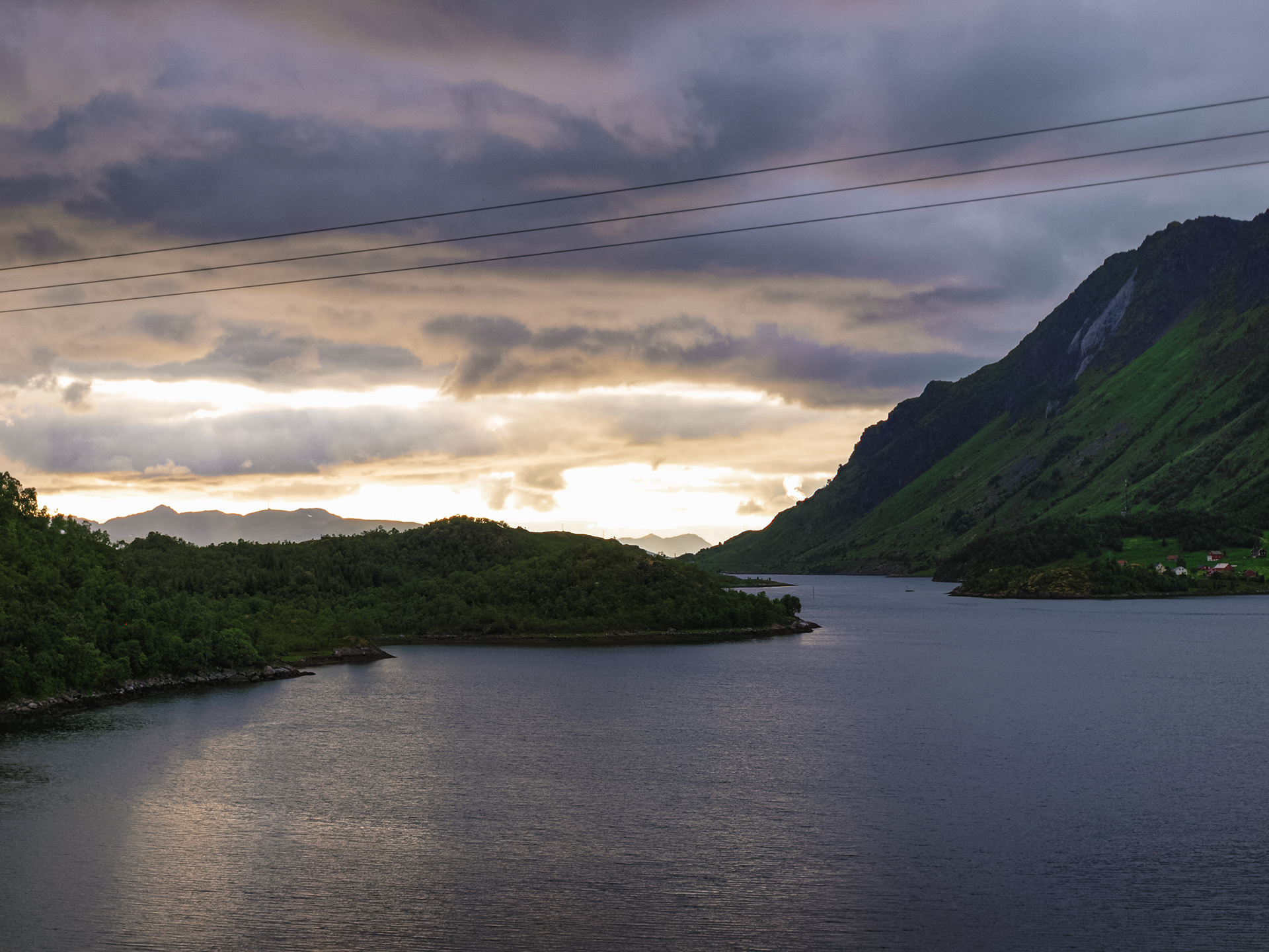 An explosion of light is visible in the distance while driving along the winding Lofoten road