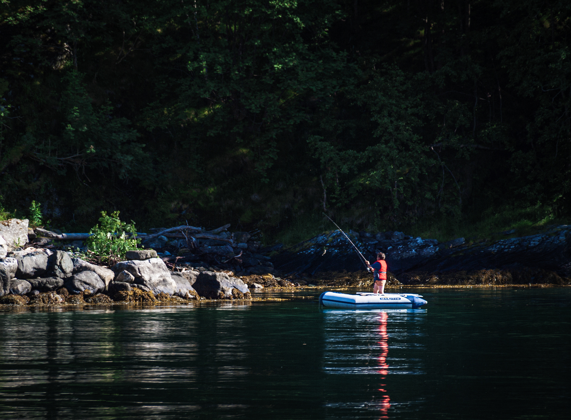 A boy excitedly reels in a fresh catch while fishing from a dinghy in Geirangerfjord