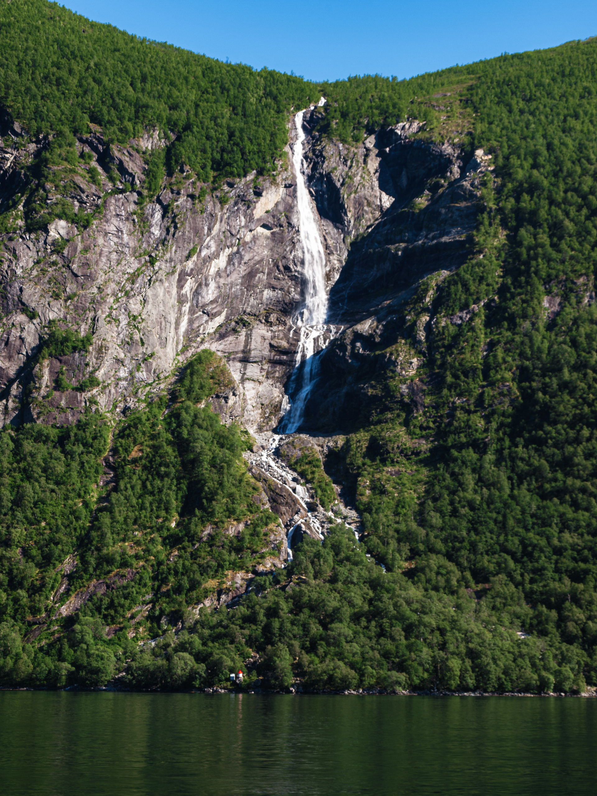 A waterfall rushes down the rock face and snakes past a small cabin