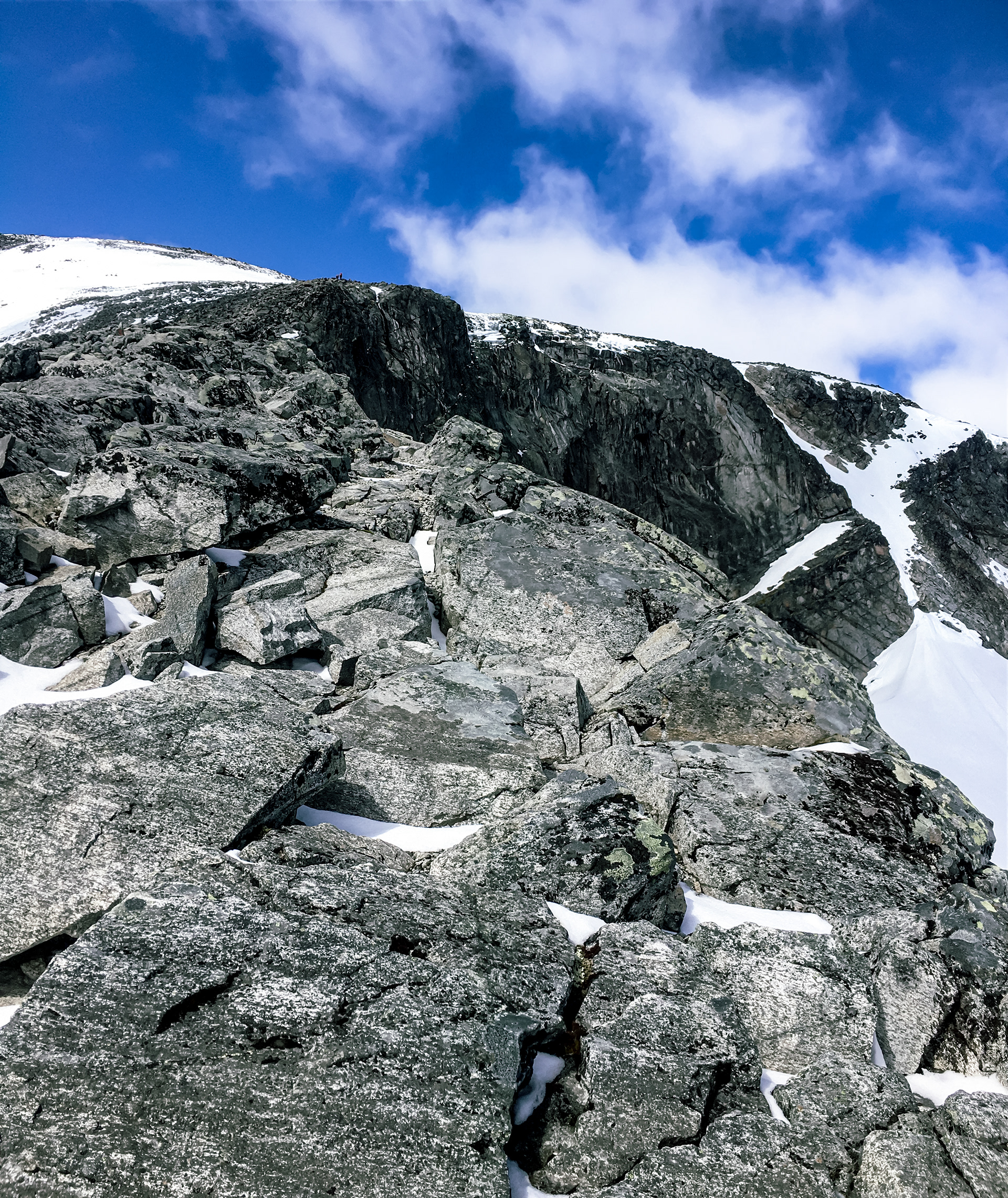 Hikers in the distance appear as tiny silhouettes against a vibrant blue sky background