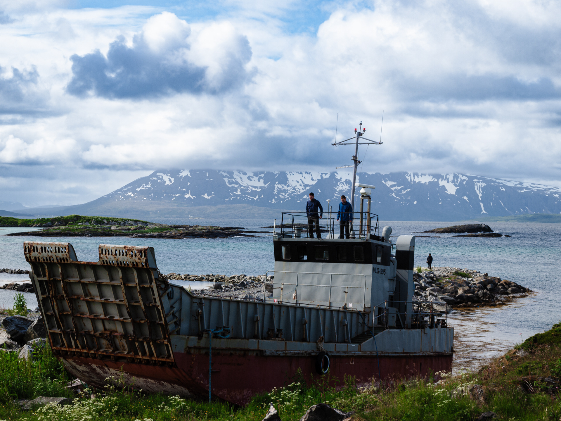 Rob and Nick gaze down from a beached landing craft while Paula looks on from a distance