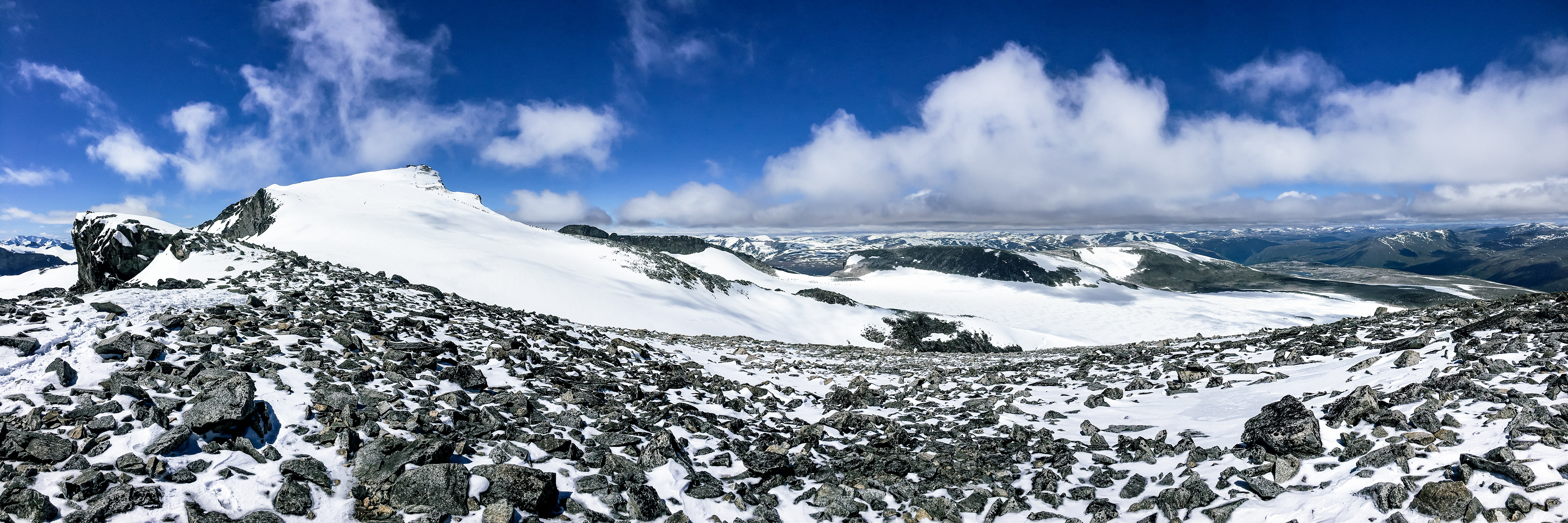 A panorama facing the other direction shows a long line of hikers from another route making their final ascent up Galdhøpiggen