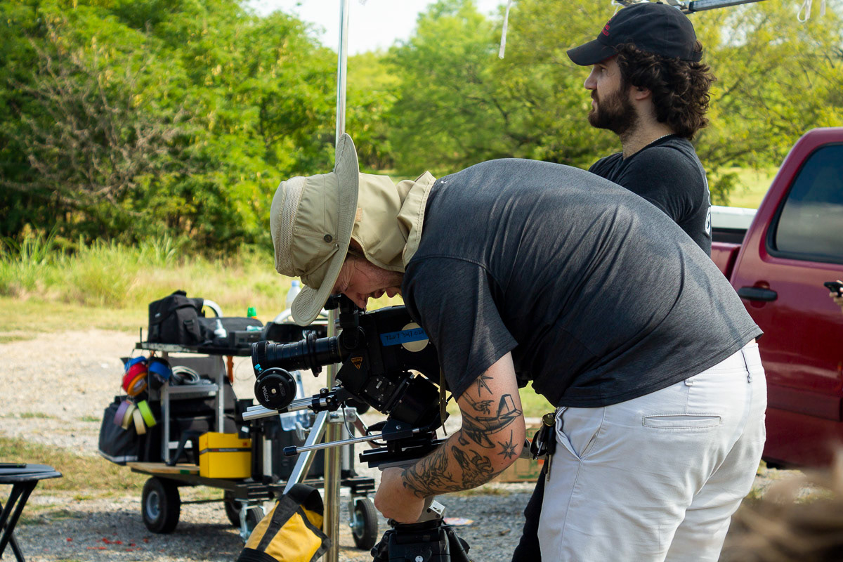 Thomas Blanks hunched over an Arri 16SRII 16mm film camera and a bearded Sam Casey behind him on the set of "Forgive Me Father" in Denton, Texas