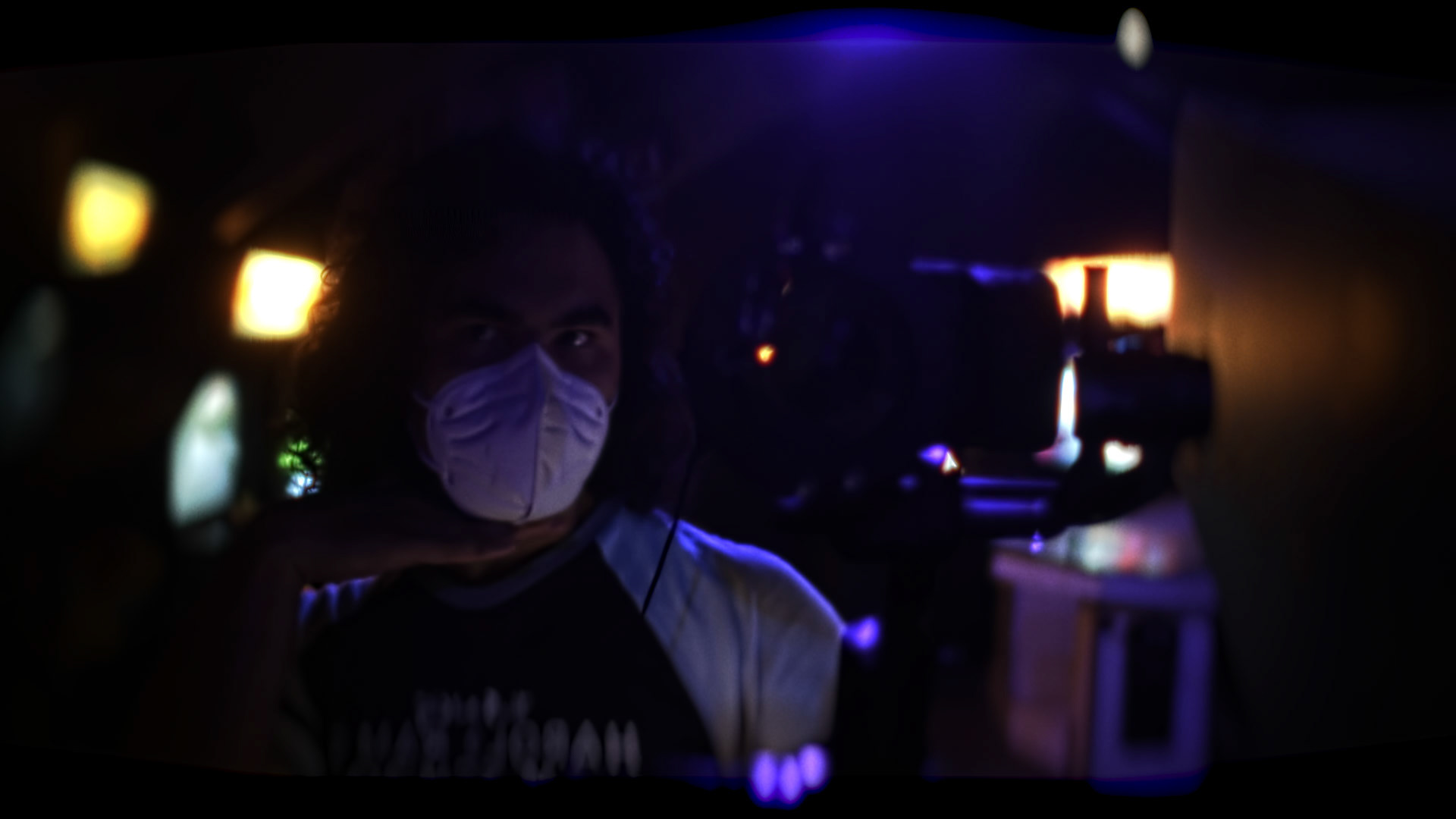Sam Casey wearing a COVID mask holding a Black Magic Pocket Cinema Camera 4K on a DJI Ronin-S stabilizer in a UV blacklight lit arcadeon the set of "Menticide"