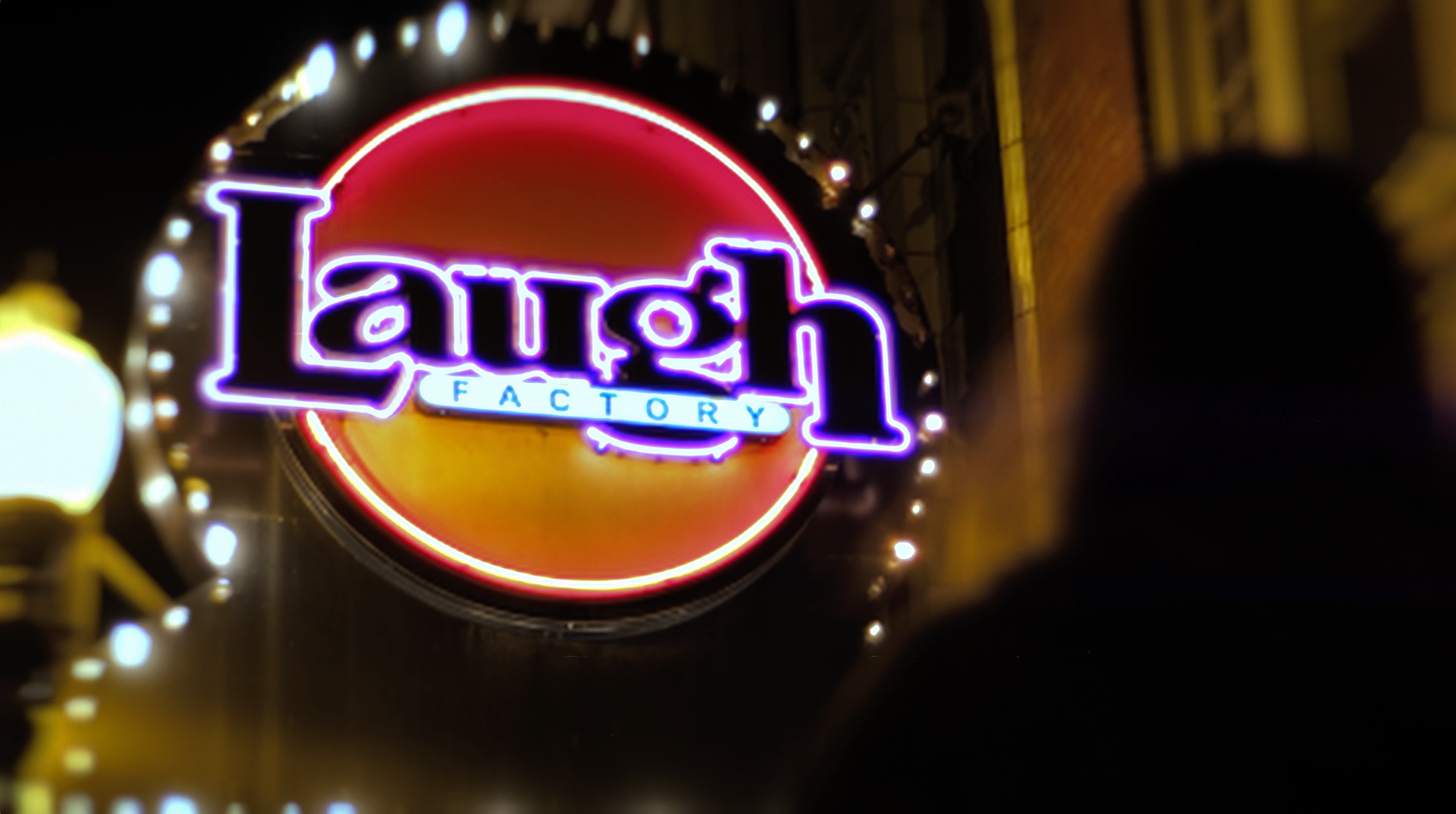 Still of a blurred Chris Higgins in the foreground in front of The Laugh Factory neon sign in "Laughing Since '79" commercial advertisement, preshow presentation, and parody of the AMC Theaters Nicole Kidman "We Make Movies Better" Advertisement by Carpe Noctem Films