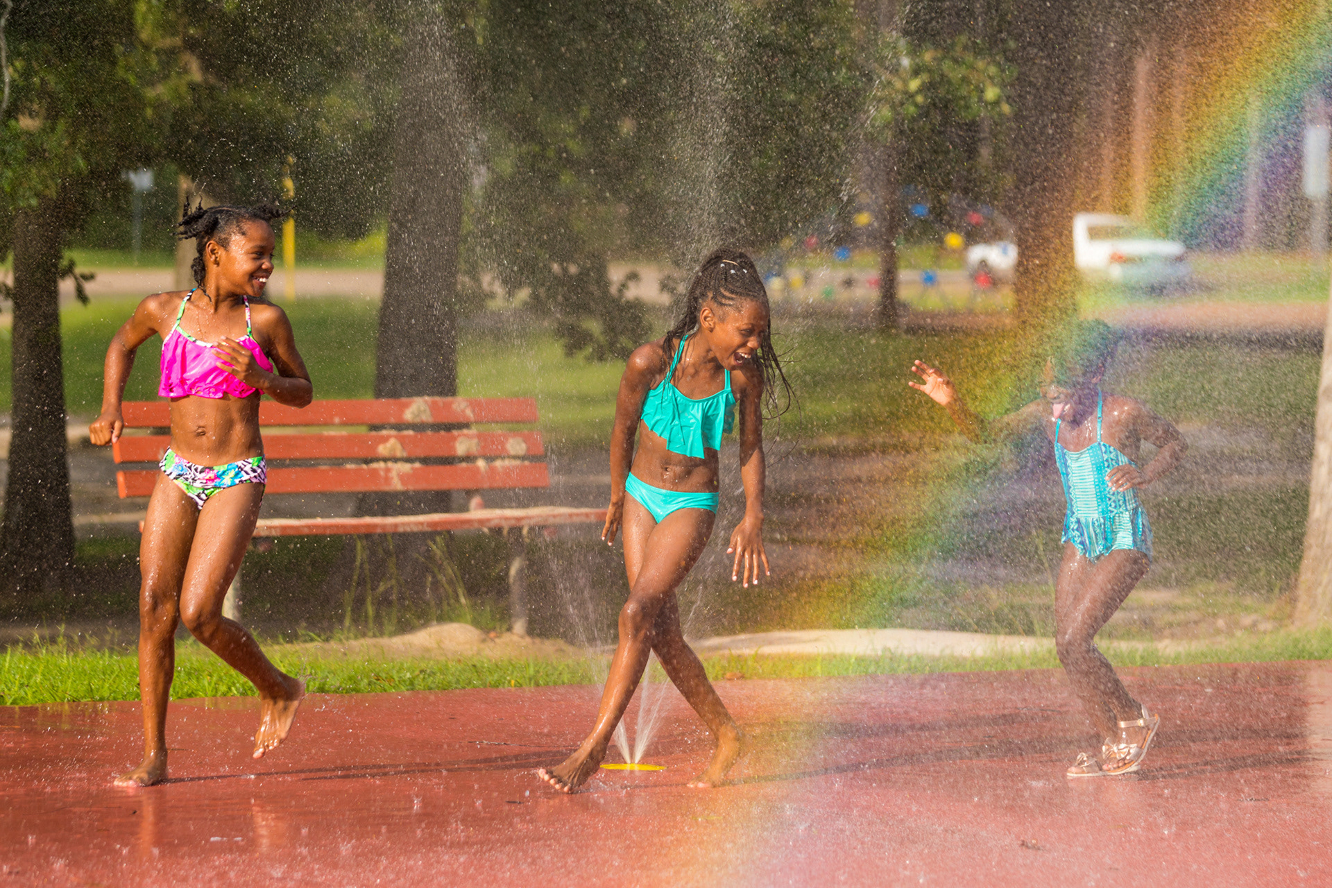 A rainbow accompanies a group of friends during a game of tag as water falls down around them Wednesday afternoon, July 11, 2018, at the Jones Park splash pad in Lufkin, Texas. Pictured from the left are Na Keyah Nicholson and sisters ZaKayla and ZaNiaya Agent. (Cara Campbell/The Lufkin Daily News)