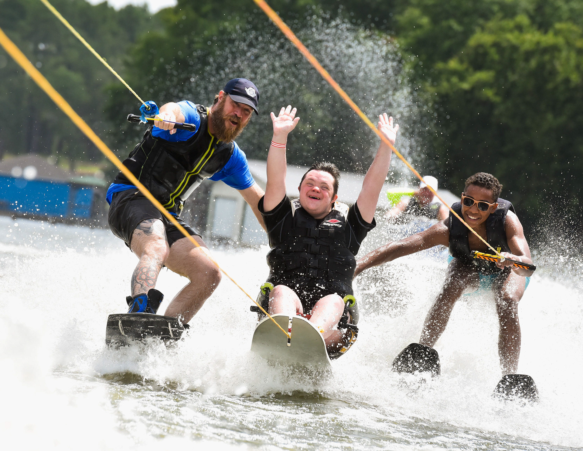 Griffin Hollowell (center), with a smile and his fists in the air, lets out a loud "Woohoo" as he wakeboards across the water with assists from from volunteer skiers Joel Raurk (left) and Jonah Chatelain during the 8th Annual Adaptive Aquafest Saturday on Lake Palestine in Bullard. The event provides wheelchair-bound adults and children access to water sports with the help of professionals. (Cara Campbell/Tyler Morning Telegraph)