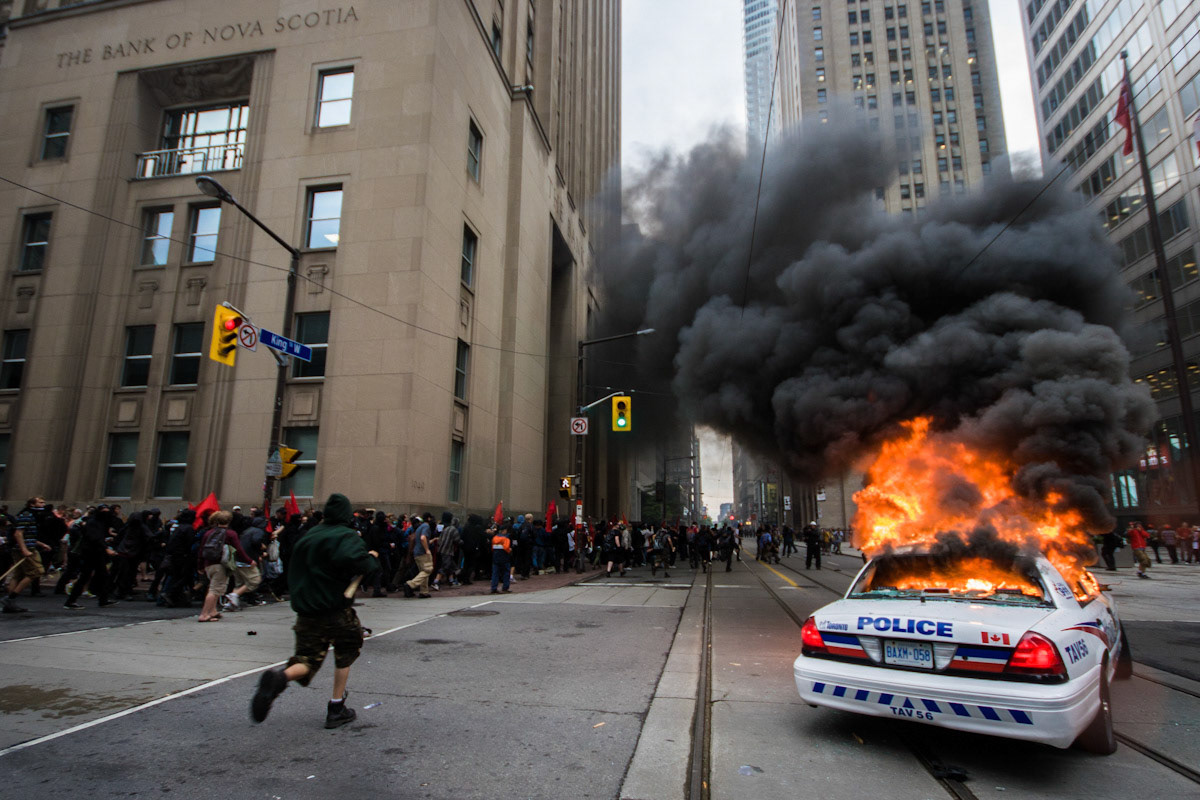 TORONTO--June 26, 2010 - Protesters rush past a burning police vehicle in the heart of the city's financial district during a major protest amid the G20/G8 Summit.