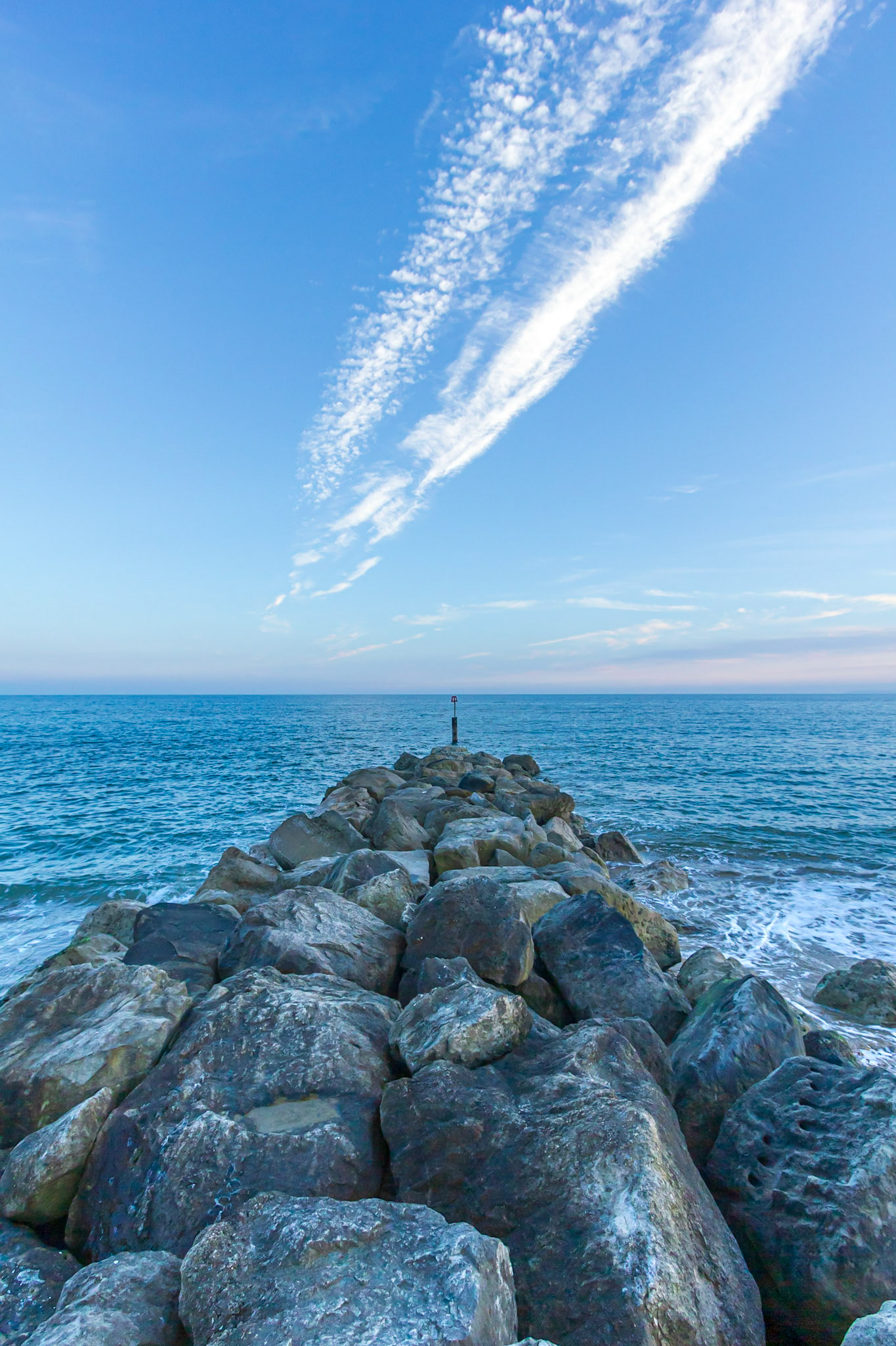 A view of a rocky groyne (breakwater) at blue hour under a majestic blue sky and white clouds