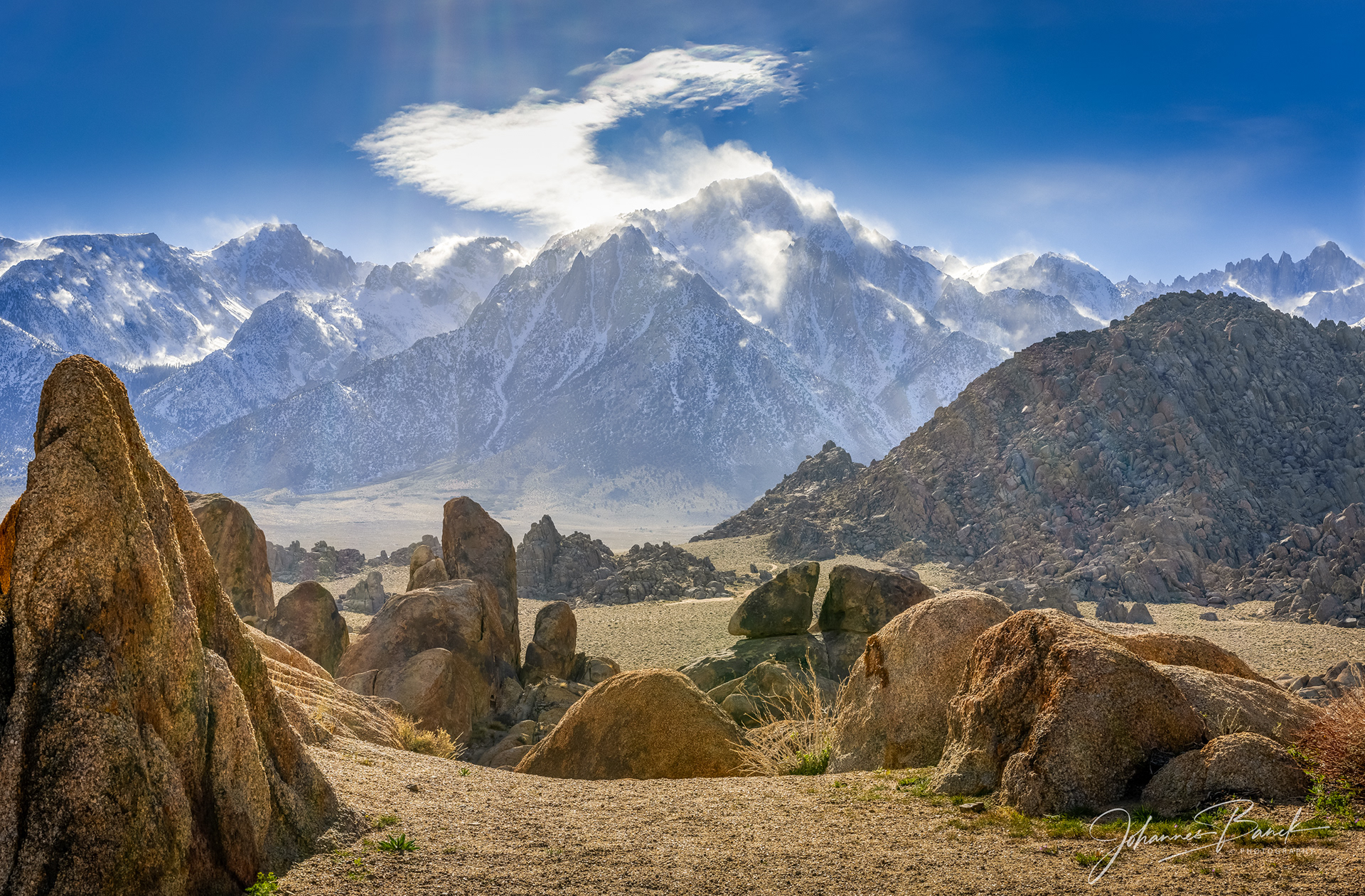 Imagine standing amidst the rugged beauty of Alabama Hills, where the ancient rock formations rise like sentinels against the vast expanse of the sky. Stepping over a small hill my search is rewarded with that perfect image. Leading lines of rock and sand guide the eye towards the majestic Sierra Nevada mountains, their snow-capped peaks piercing the heavens. The scene is a symphony of light and shadow, a testament to nature’s artistry, where every element harmonizes to create a breathtaking tapestry of color and form. This is a place where the soul finds solace, and the spirit soars, enveloped in the serene embrace of the wild.