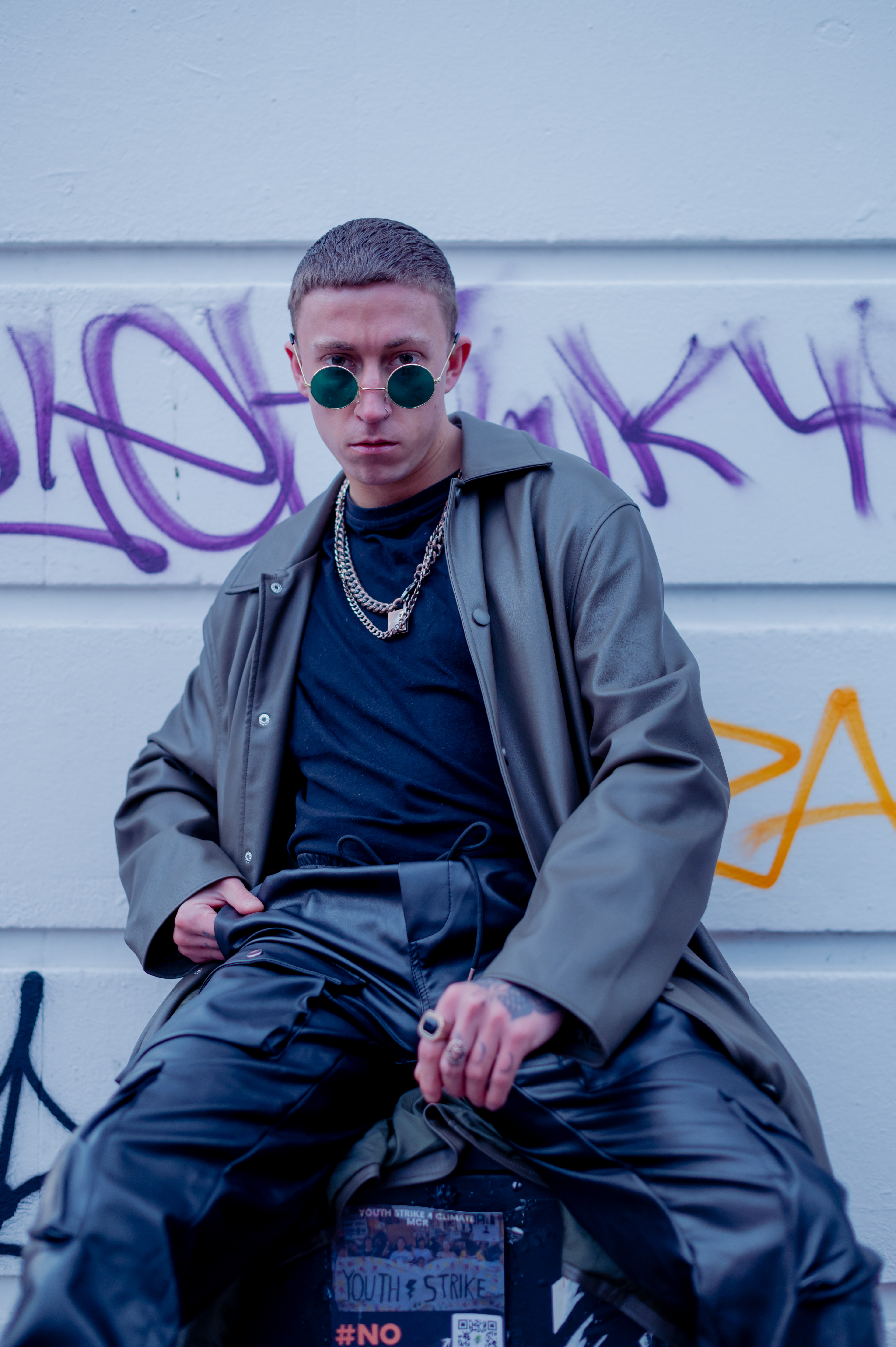 Man in boots, long leather jacket, leather pants, black t-shirt and chains, in Manchester - Northern Quarter , with sunglasses and rings 