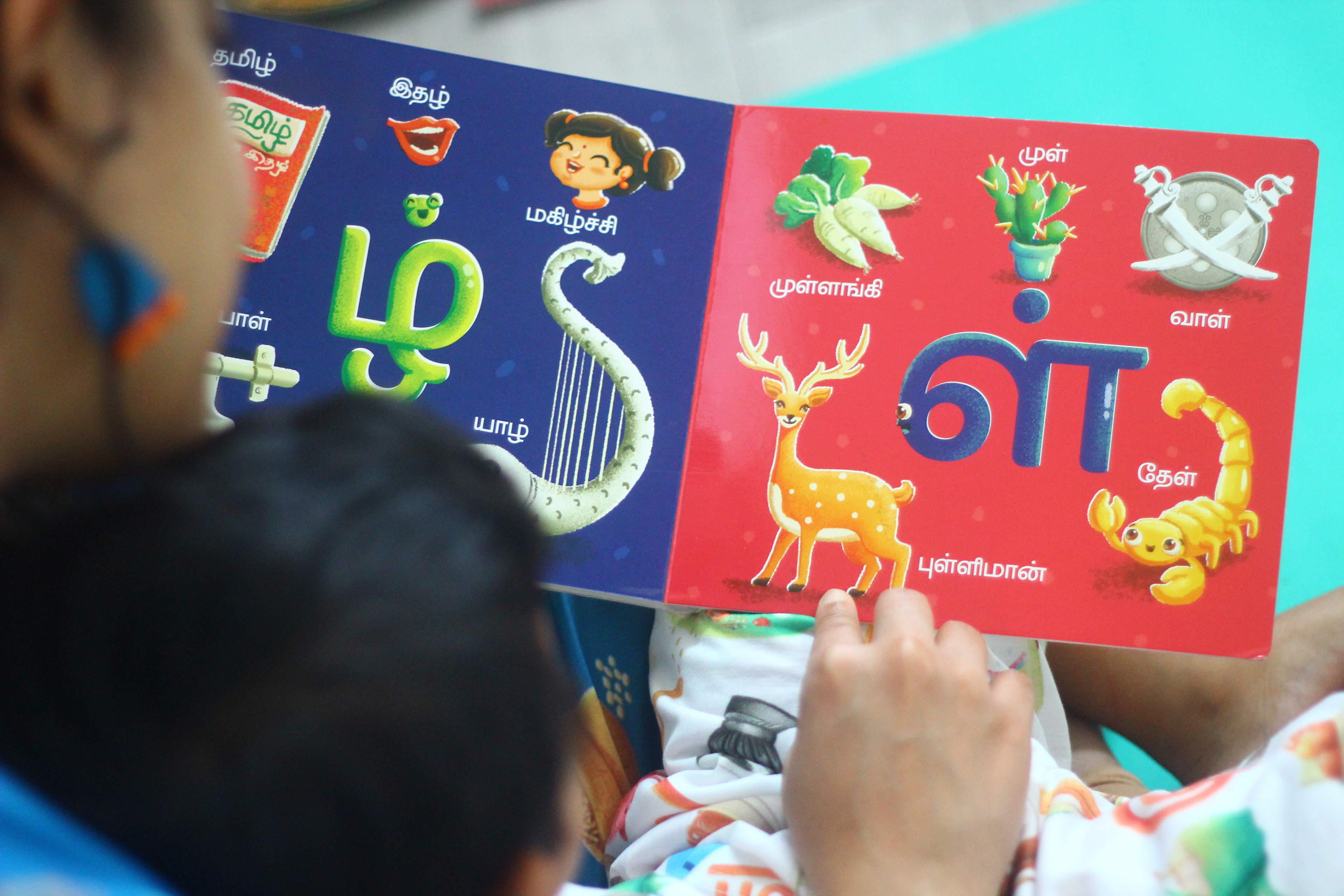 Vidhaippom Meithamizhai Tamil alphabet board book: child turning pages to the zha and la spreads