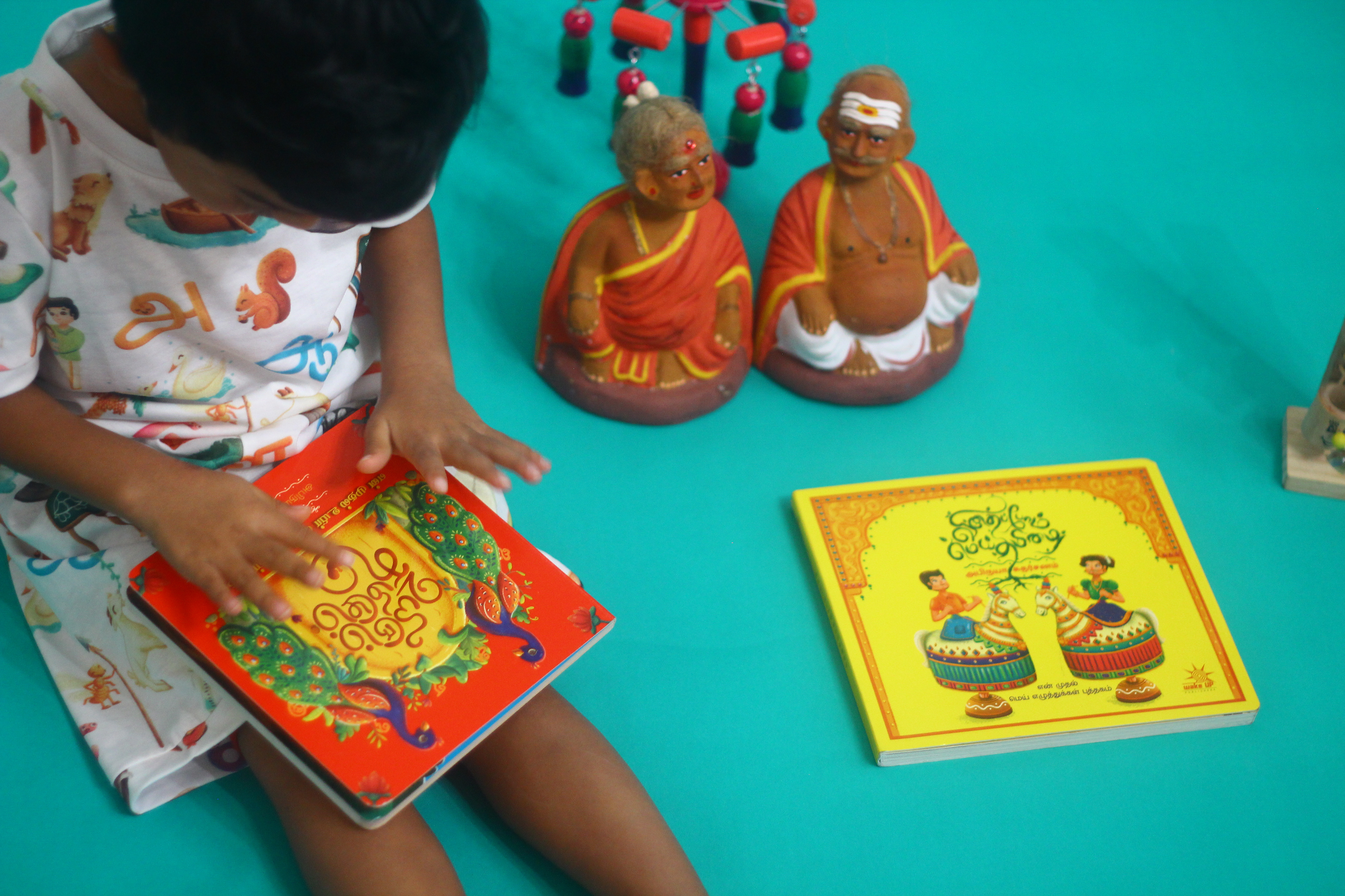 Uyirum Tamizhum Tamil vowels board book: child reading beside clay dolls
