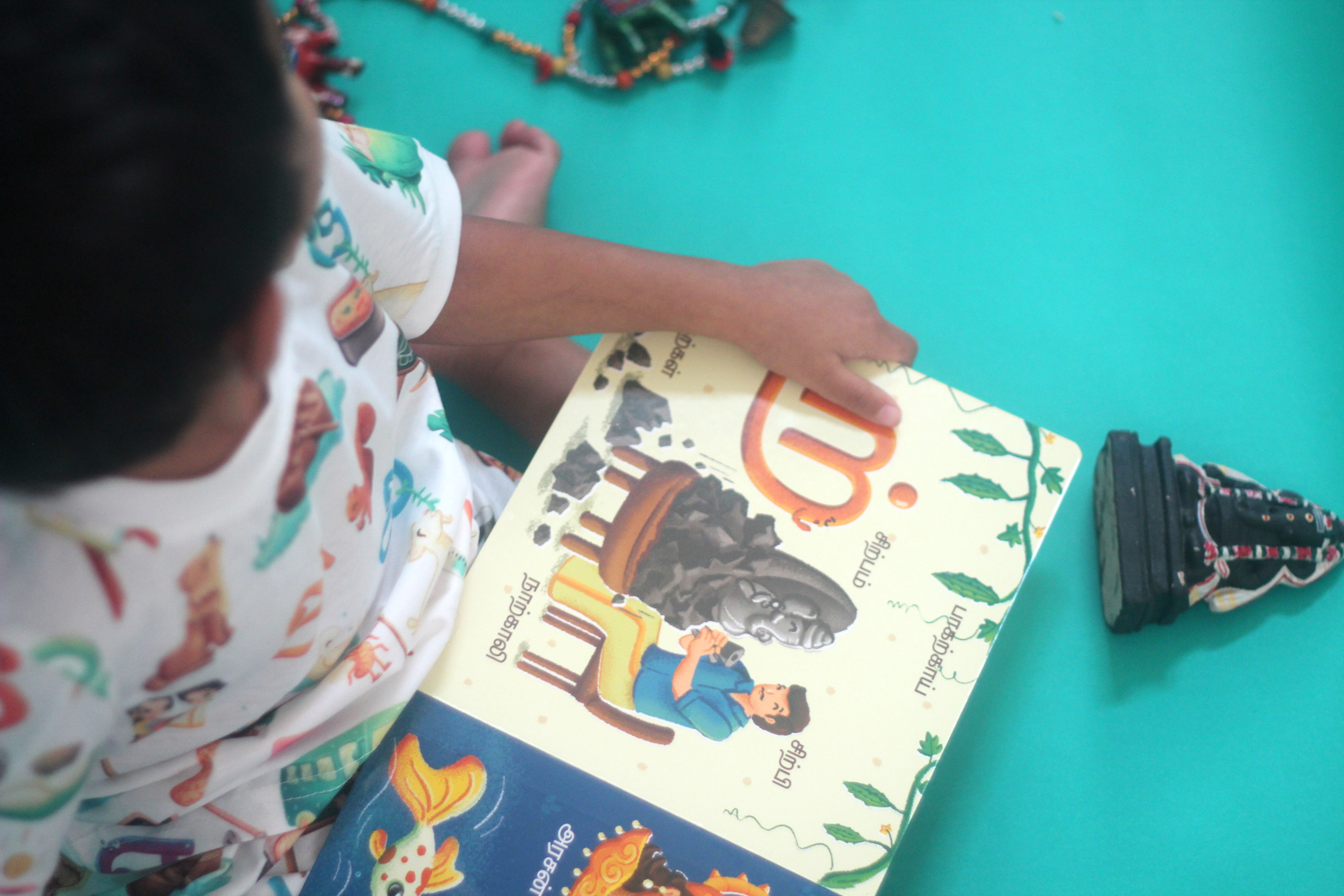 Vidhaippom Meithamizhai Tamil alphabet board book: child reading the board book on teal