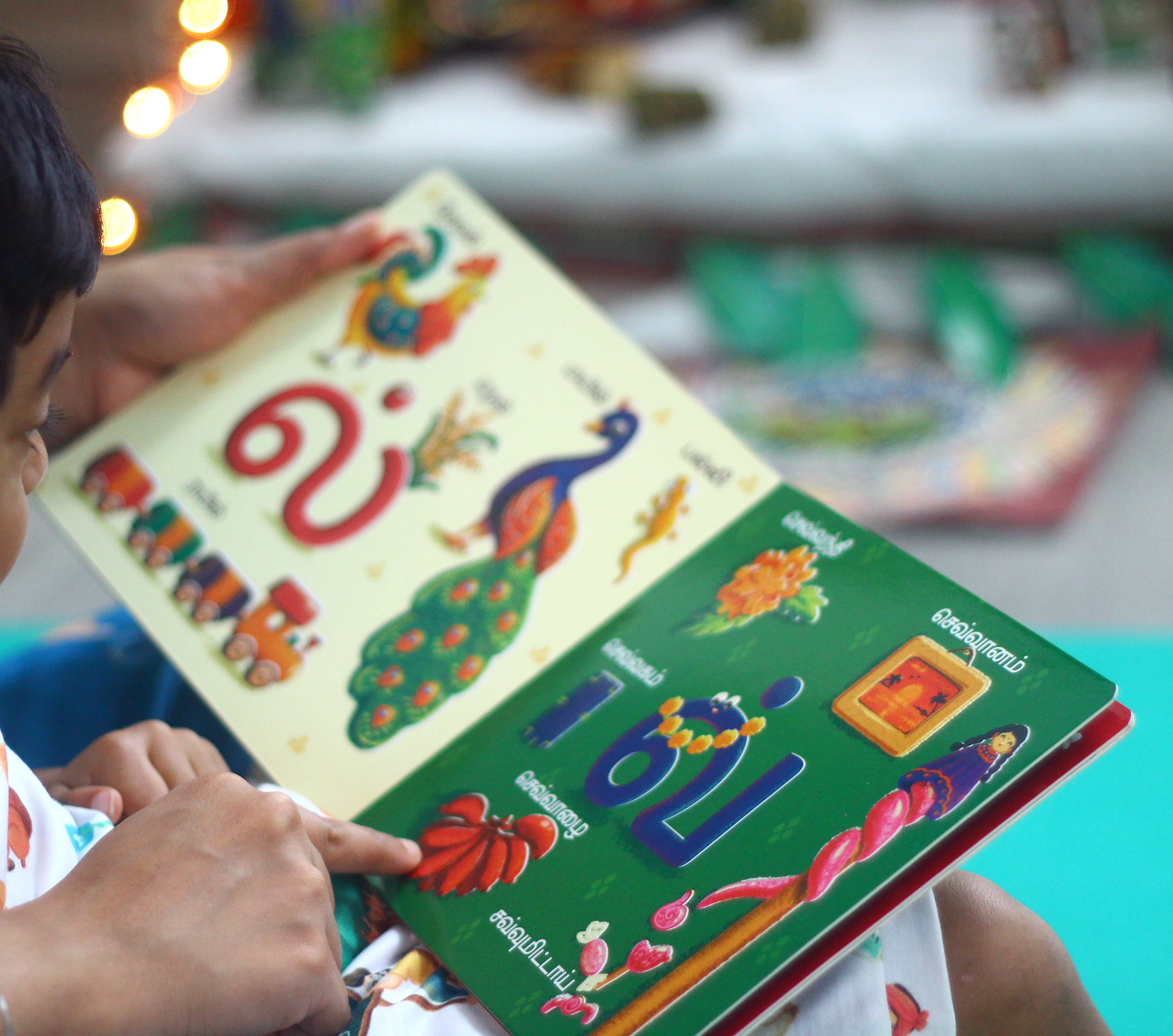 Vidhaippom Meithamizhai Tamil alphabet board book: child reading the board book outdoors