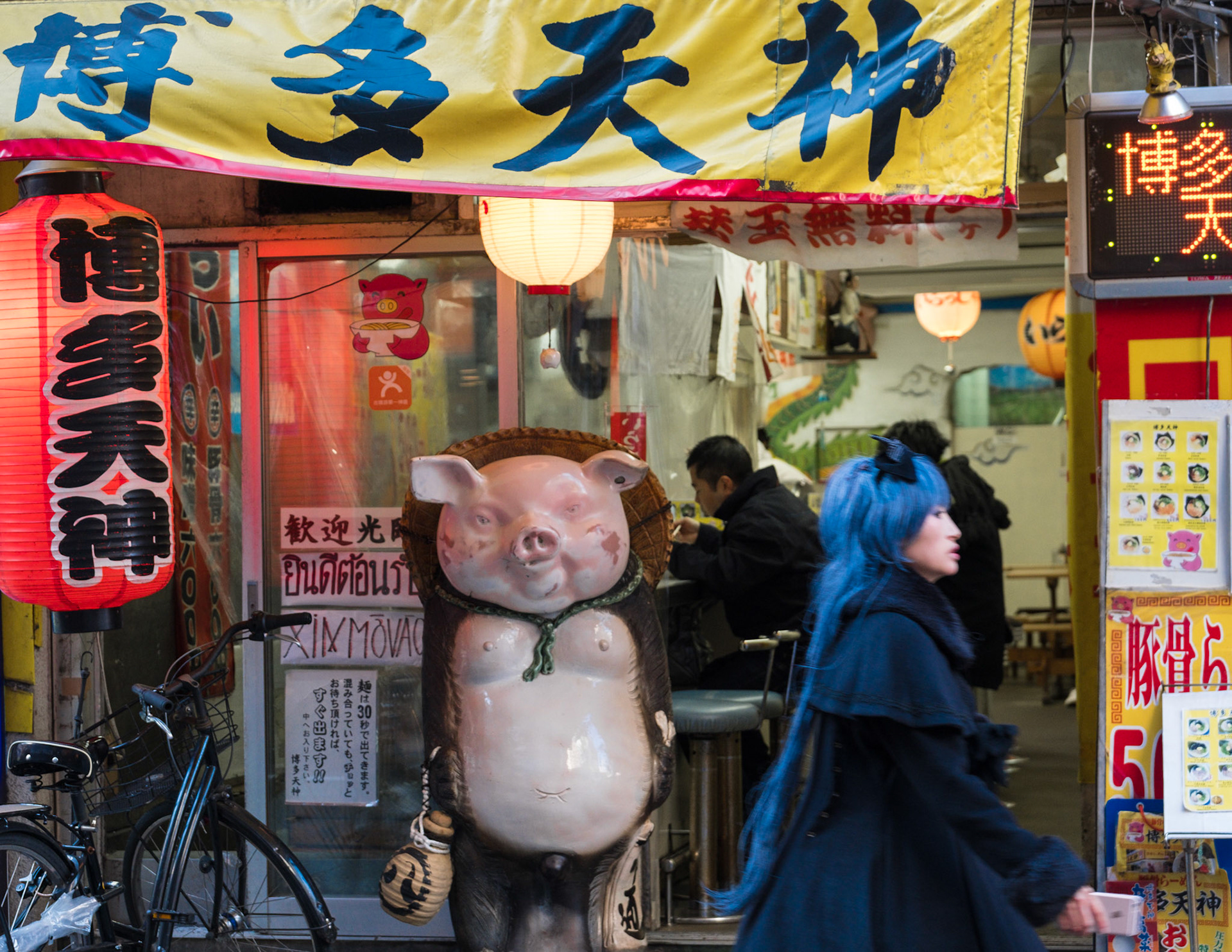 Woman walking past a Tokyo diner with a pig statue.