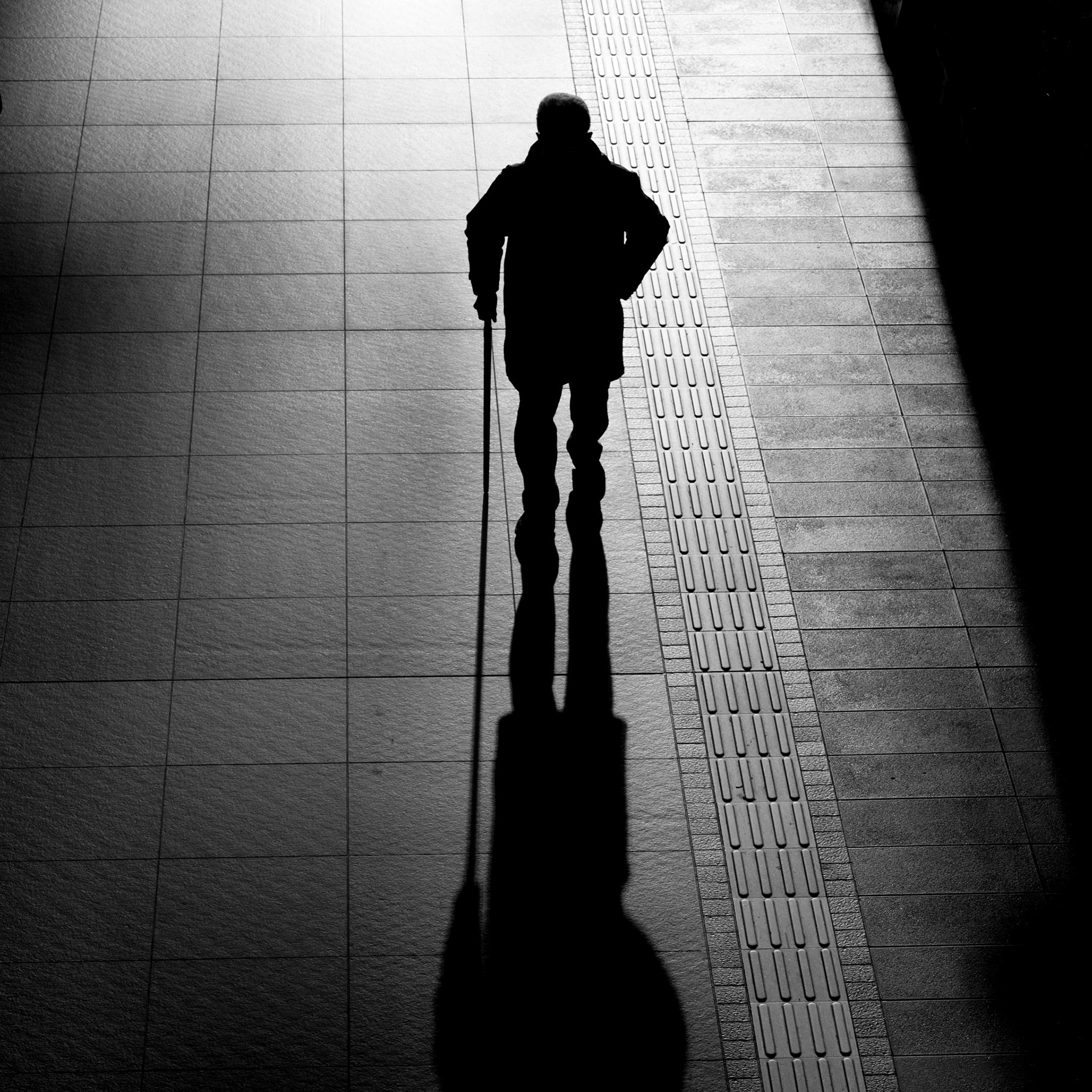 A silhouette of an elderly man walking through Kyoto Station using a cane.