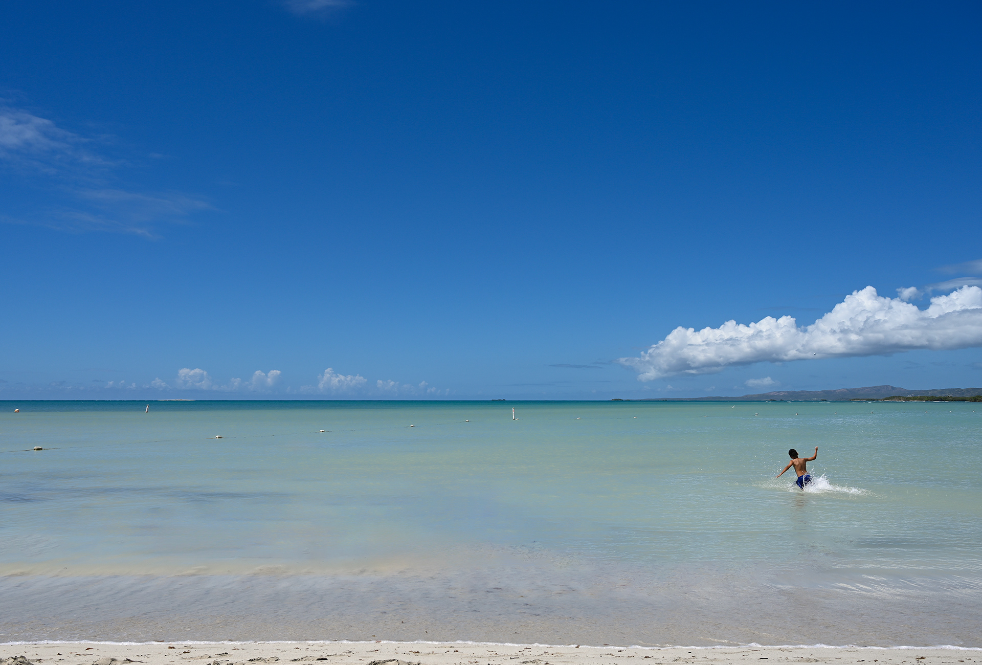 A joyful moment captured as a child jumps into the calm, turquoise waters of the Caribbean ocean at Playa Santa Beach in Guánica, Puerto Rico. The clear blue sky and serene atmosphere make this the perfect family-friendly beach destination.