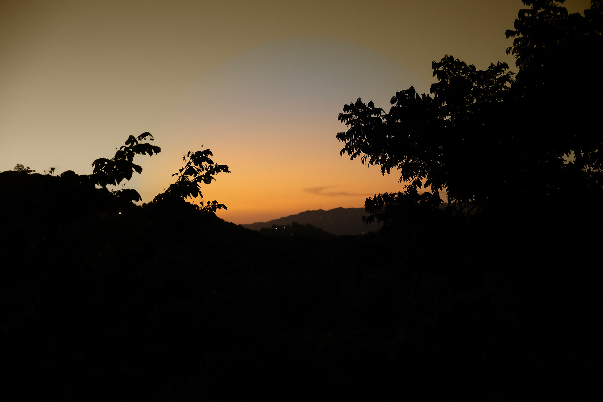 Golden sunset over lush tropical hills at Hacienda Eterna Primavera, with the ocean visible in the distance, creating a peaceful and breathtaking view.