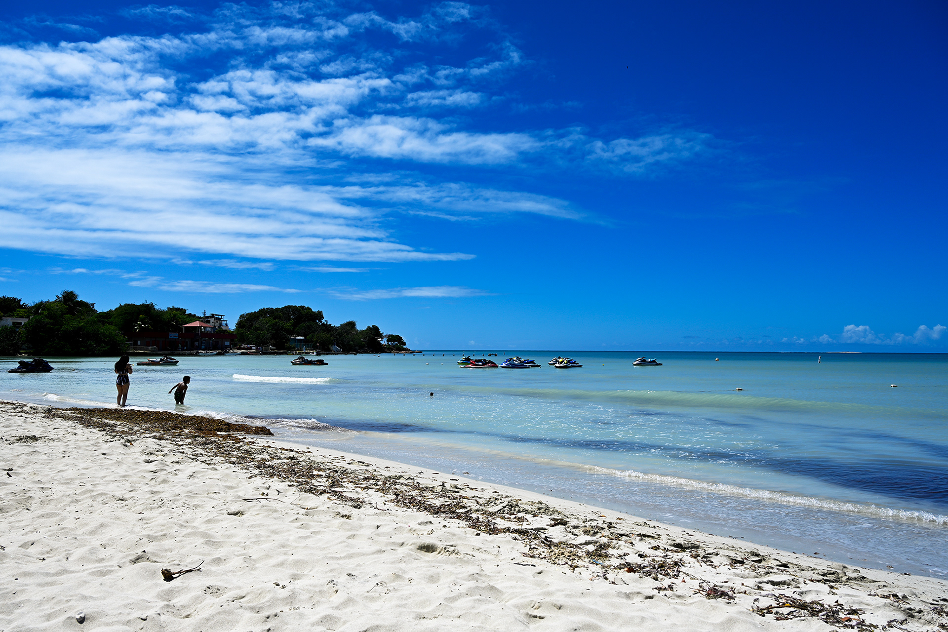 A peaceful view of Playa Santa Beach's white sand shore stretching out to the calm, turquoise waters of the Caribbean. The serene atmosphere, combined with a blue sky, makes it a perfect place to relax and unwind.