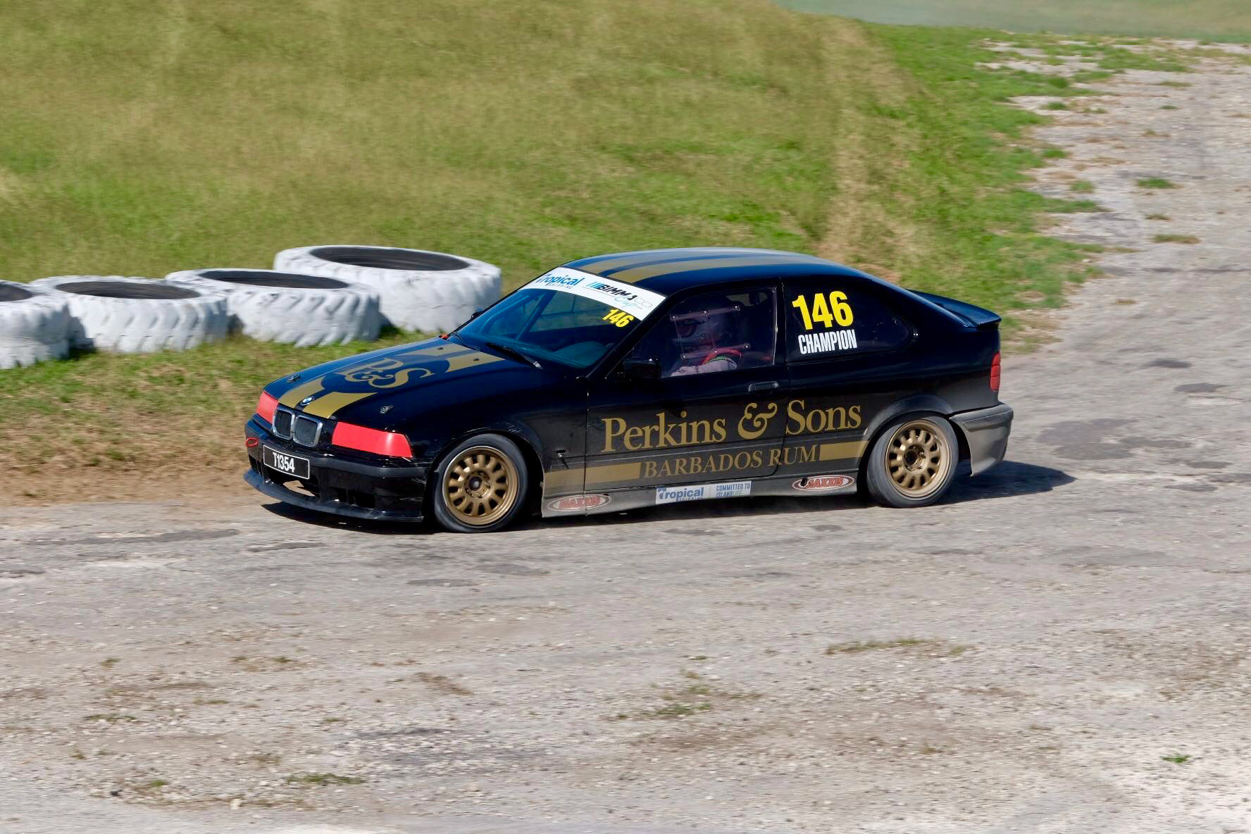 Perkins & Sons-sponsored rally car racing at Rally Barbados, black livery with Perkins & Sons branding on a gravel track