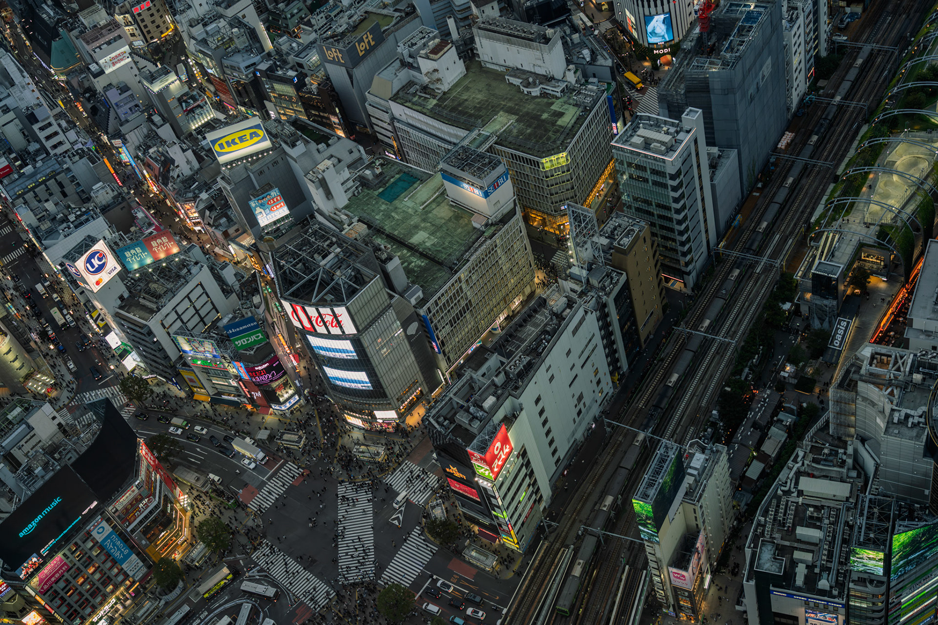 Pedestrians cross Shibuya scramble crossing in Tokyo as commuter trains pull into the station