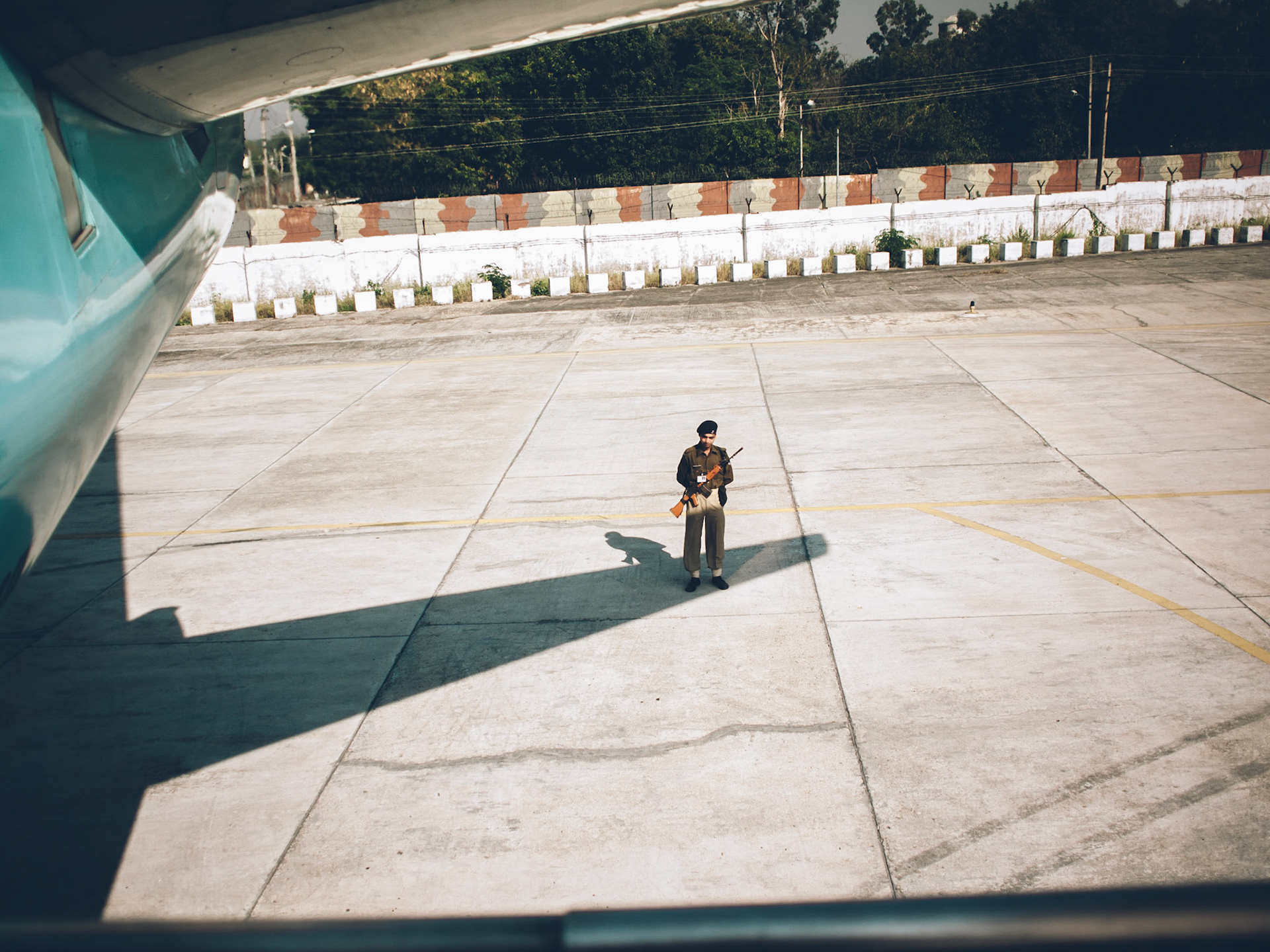 A soldier stands in the shade of the wing of an aircraft that has just landed in Jammu airport.