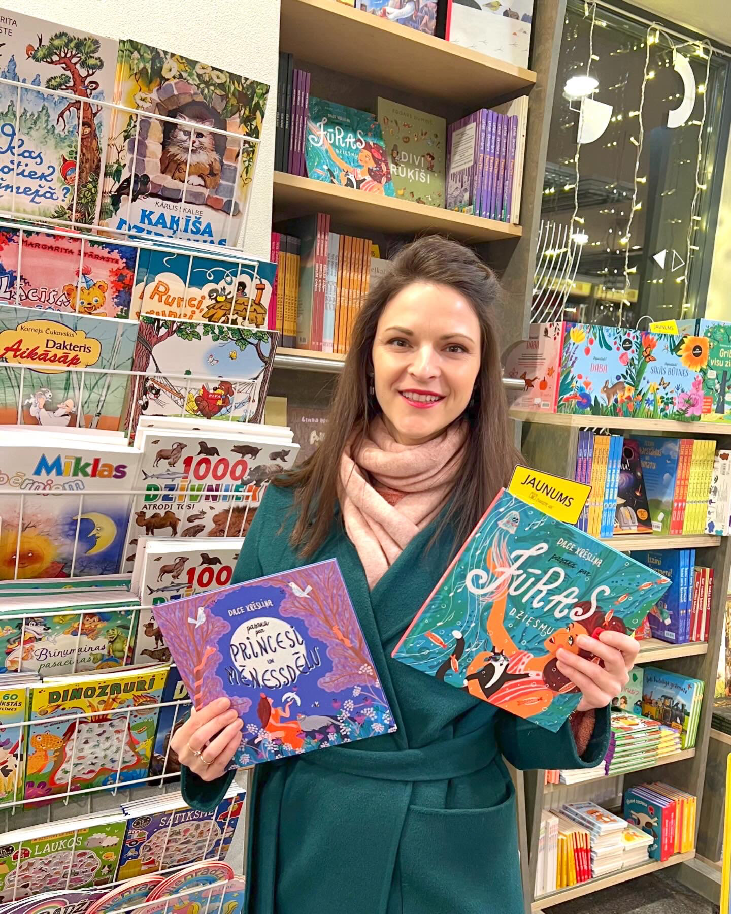 Autore Dace Krēsliņa, turot rokās abas savas grāmatas - Pasaka par Jūras dziesmu un Pasaka par Princesi un Mēnessdēlu