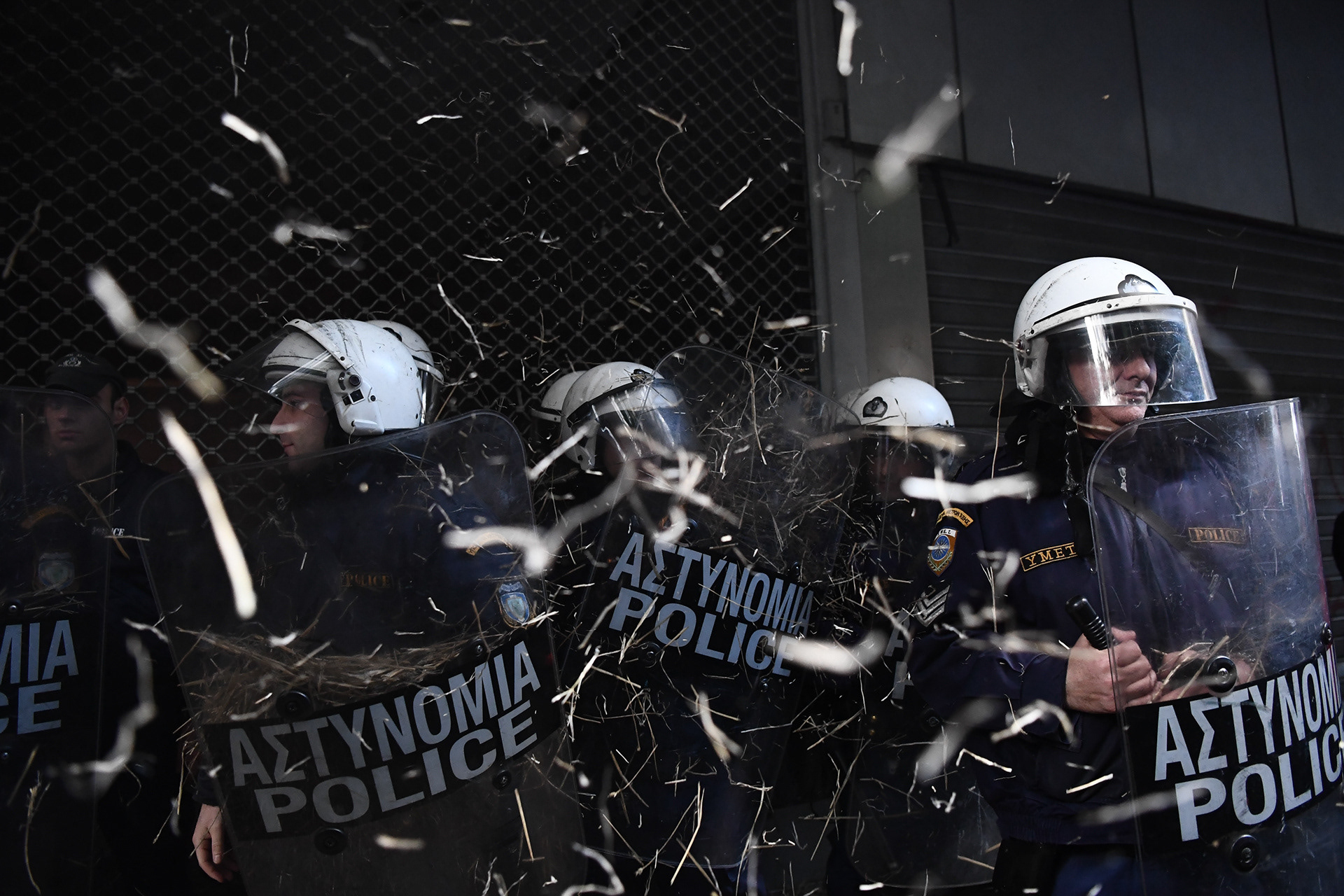 Riot police officers stand, as protesters throw hay at them during a protest outside the Ministry of Finance, in Athens, Greece, on Thursday, Nov. 22, 2018.