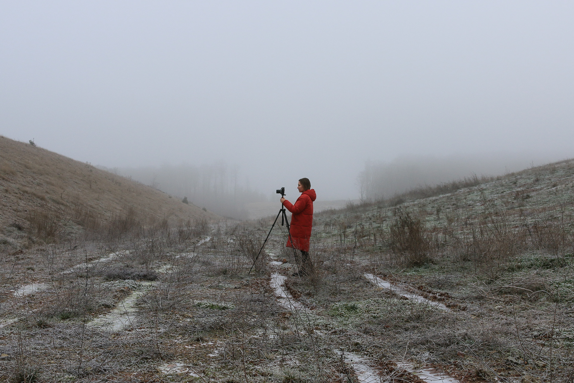 Selbstportrait der Künstlerin Anna Bergold in einer Landschaft stehend mit Kamera und Stativ 