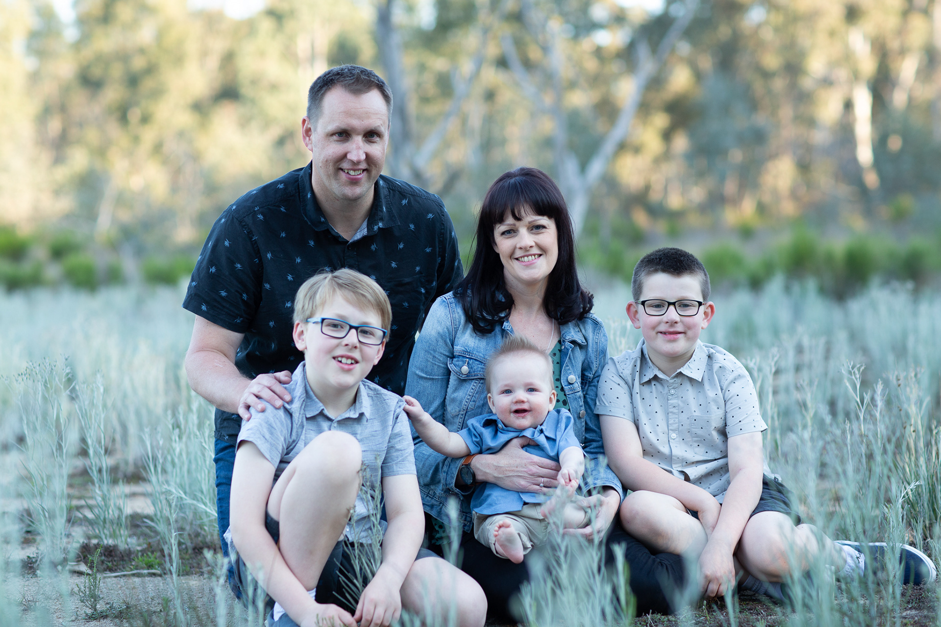 Family portrait of a mother and father with three boys with a bush background