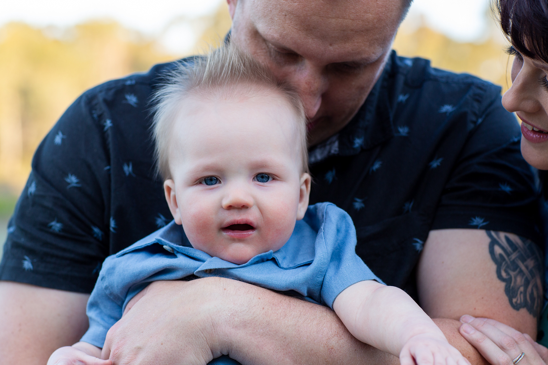 Close up photograph of baby boy in the arms of his father and mother looking in