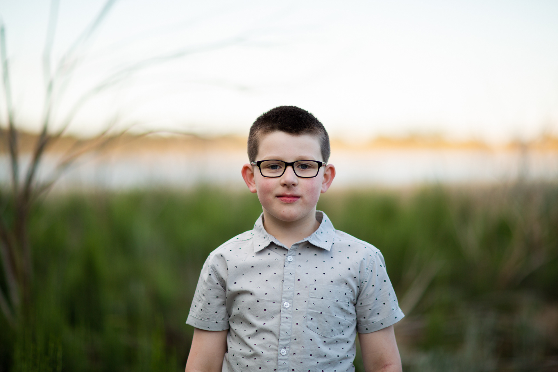 portrait photo of a boy in a shirt with water and tree background
