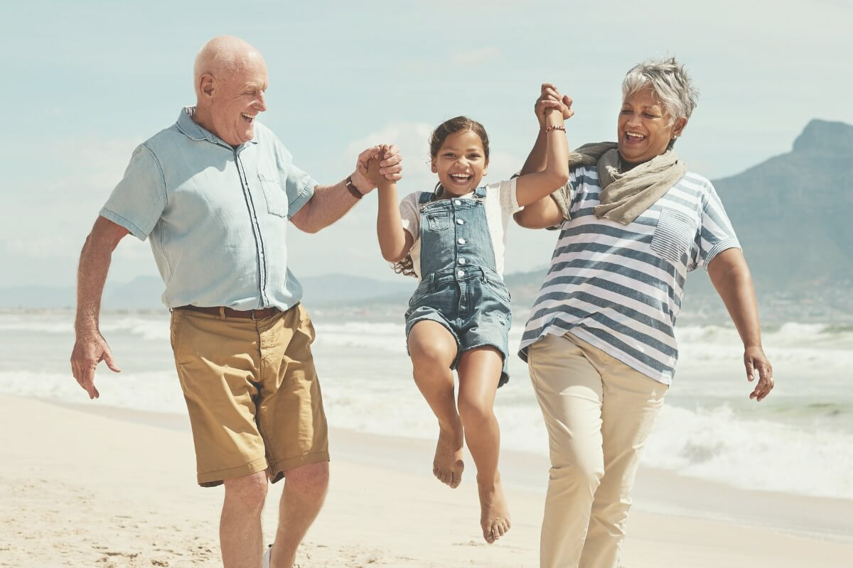 Photo of grandparents playing on the beach with their granddaughter
